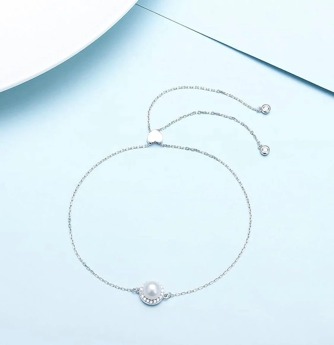 Silver jewelry set including a necklace with a pearl pendant and matching earrings with small round stones, arranged on a light blue surface.
