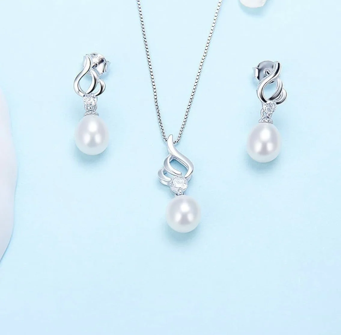 Pearl jewelry set including a necklace and matching earrings with silver swirl design and embedded diamonds, displayed on a light blue background.