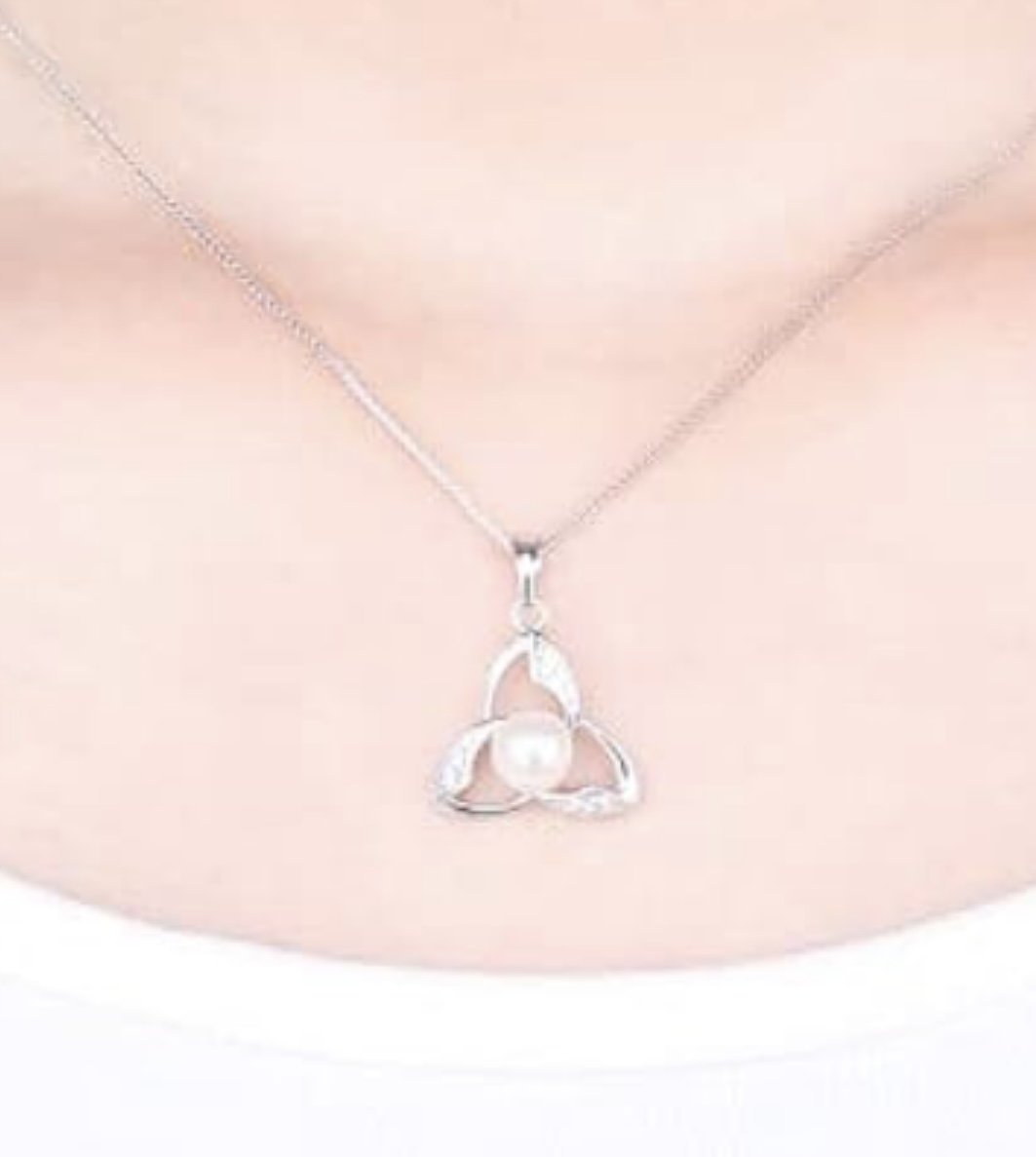 Close-up of a woman's neck wearing a delicate silver necklace with a pendant shaped like a blooming flower with a pearl at the center.