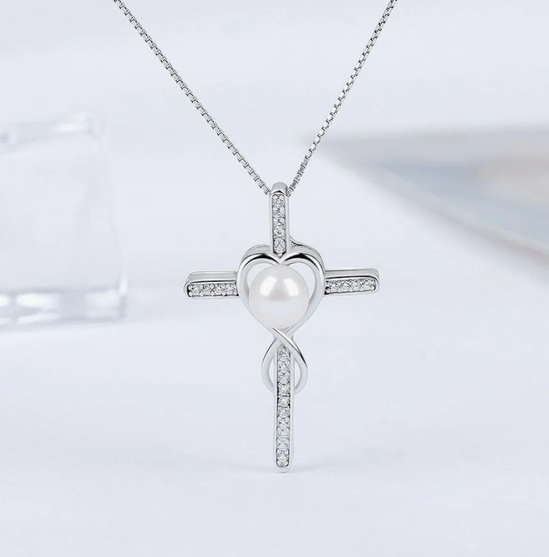 Silver cross pendant necklace with a pearl at the center and small diamonds embedded in the cross.
