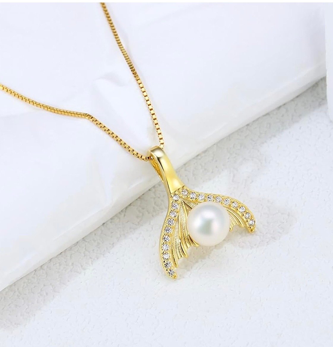 Gold necklace with a pendant shaped like a fish tail, decorated with small diamonds and a central pearl.