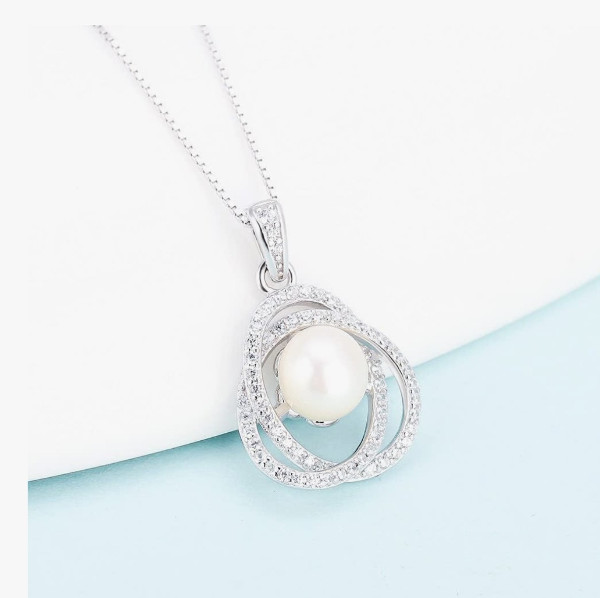 Silver necklace with a pearl pendant and diamond accents, resting on a white and light blue background.