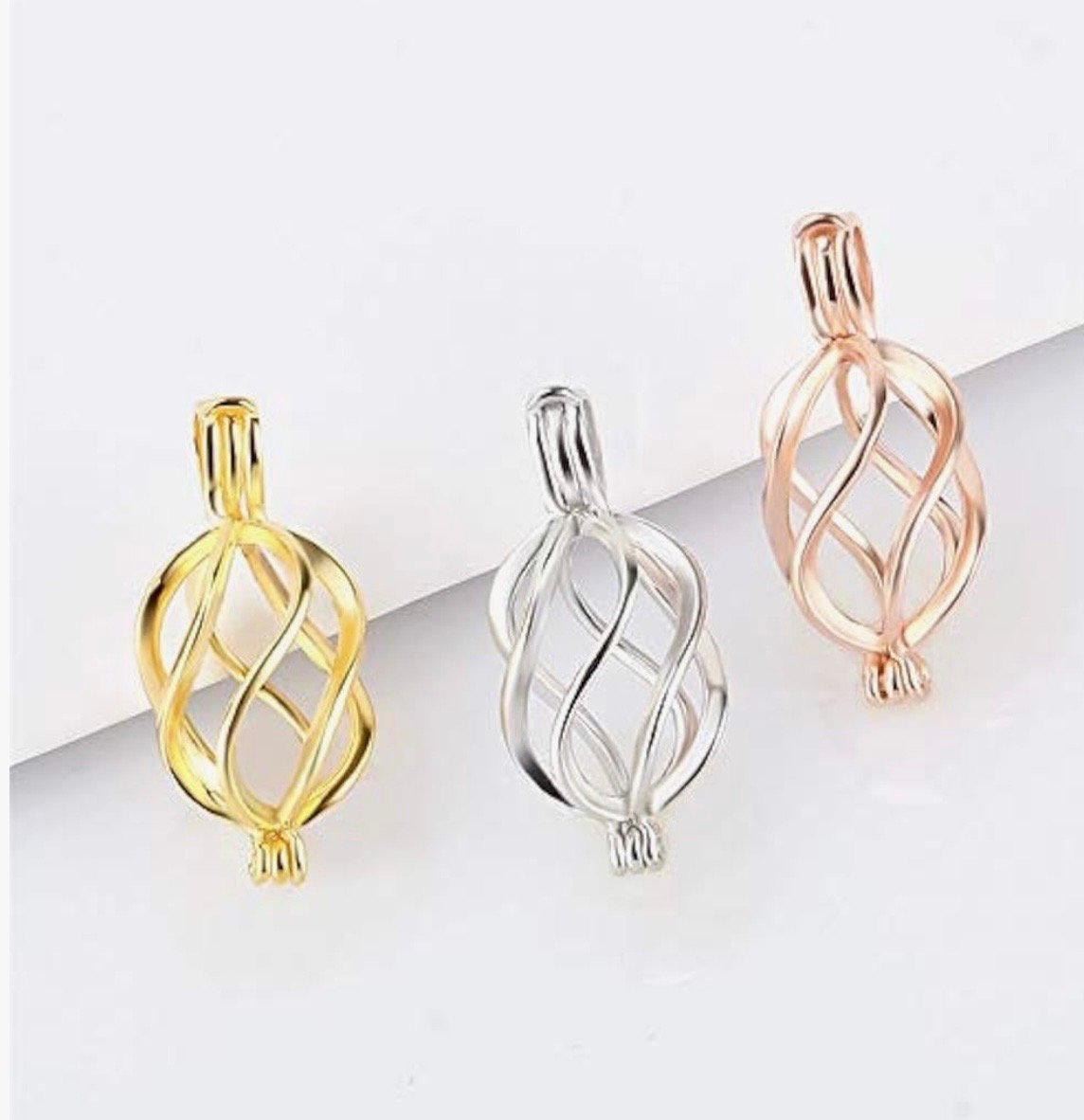 Three decorative metallic pendant charms in gold, silver, and rose gold colors, each with a twisted, openwork design, placed on a white surface.
