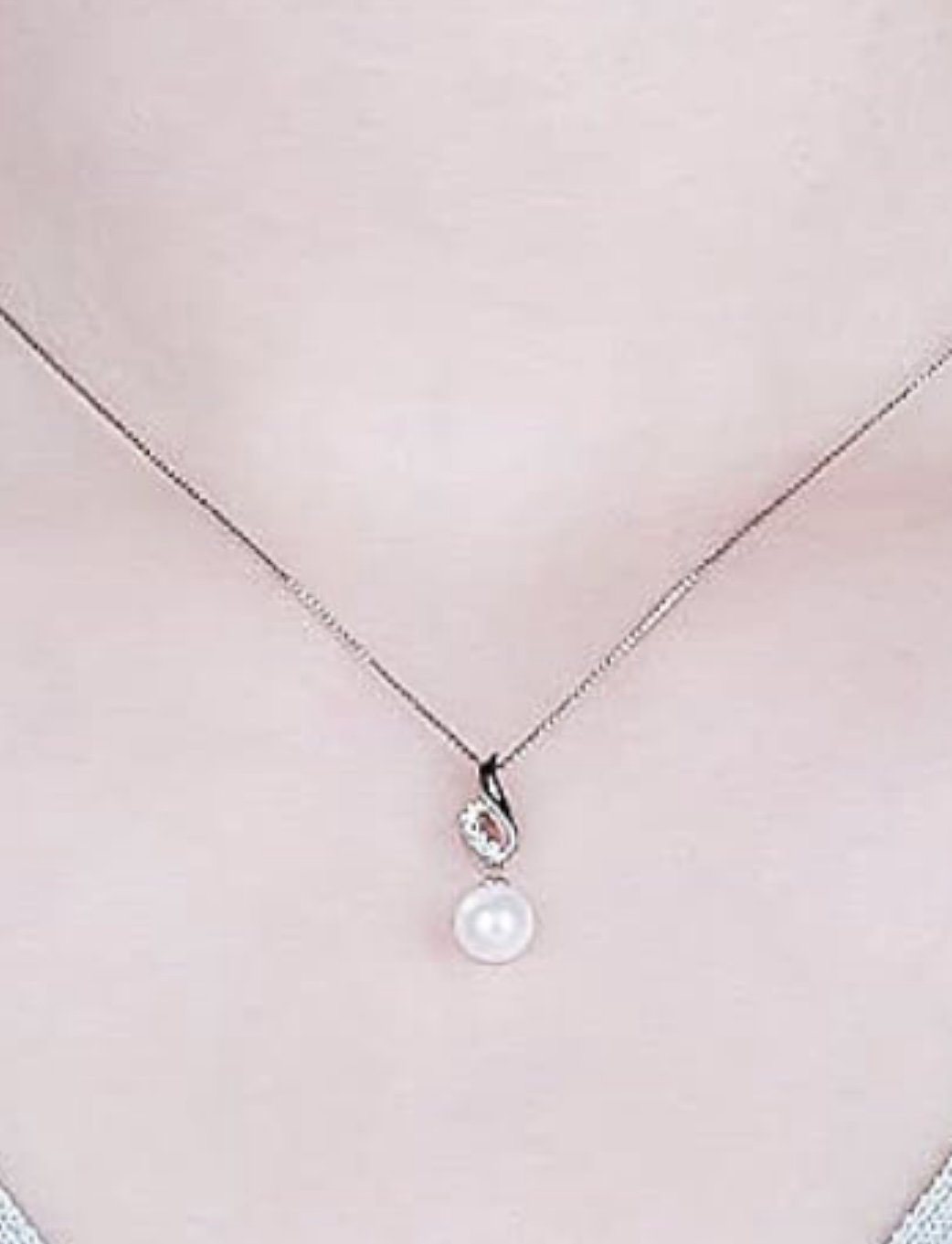 A close-up of a person's neck wearing a delicate necklace with a pearl pendant and small gemstone accent.