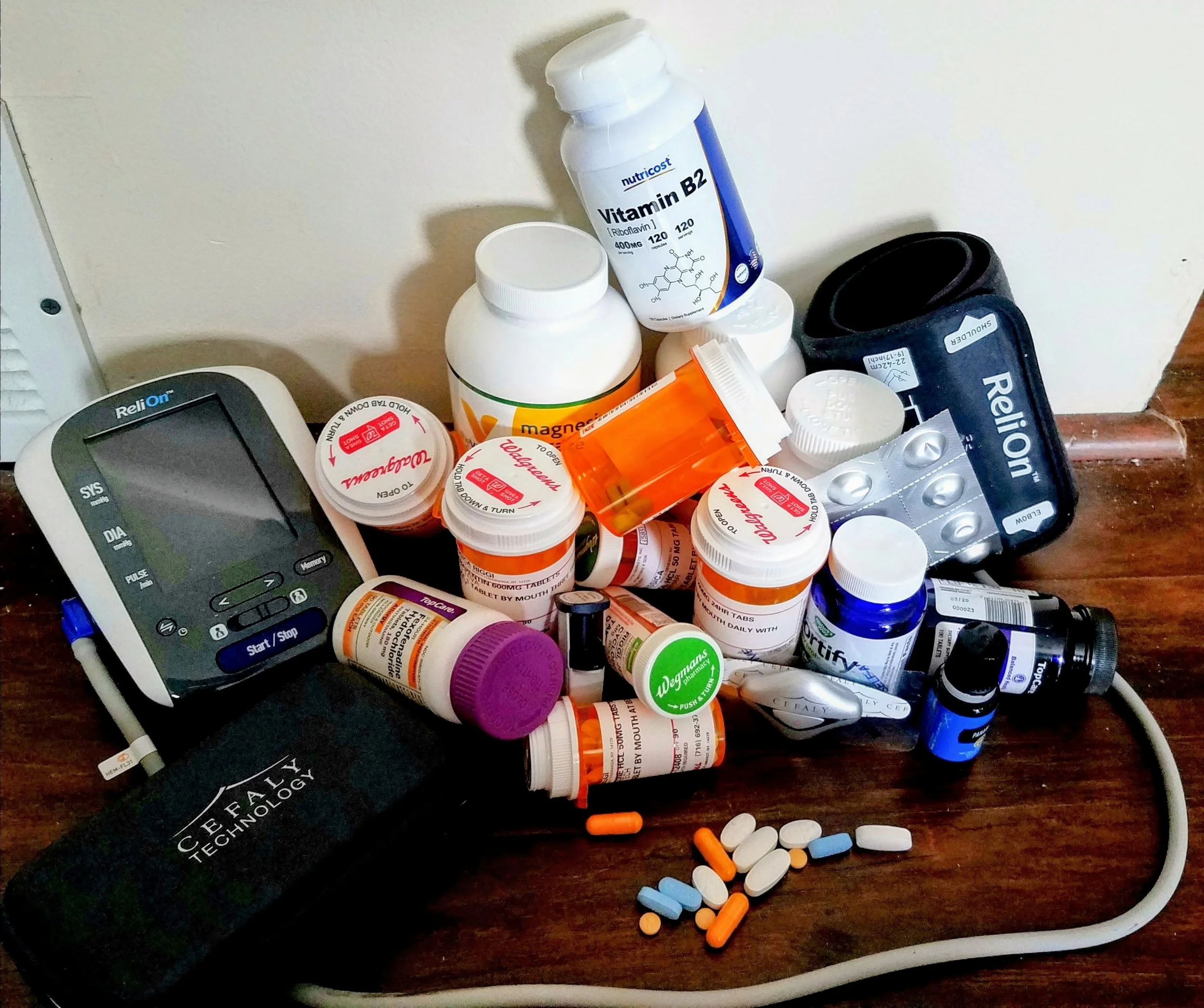 A collection of various prescription medication bottles, pills, and tablets on a wooden surface, alongside a blood pressure monitor and a digital timer. Represents the multitude of treatments someone must keep track of when living with dysautonomia.