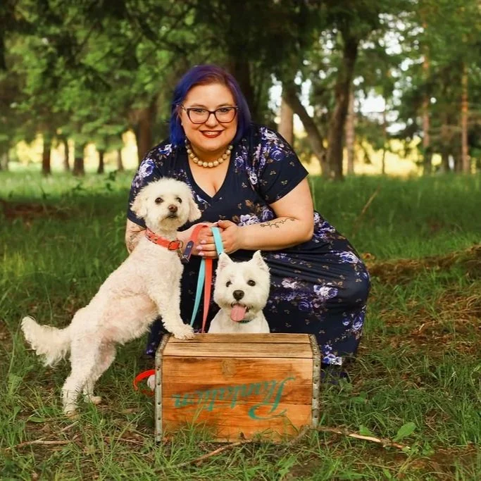 A picture of Jessica Allen LCSW with her therapy dog Riley on the left wearing a pink collar and Westley in front of her with tongue out wearing a blue collar as her therapy dog in training.