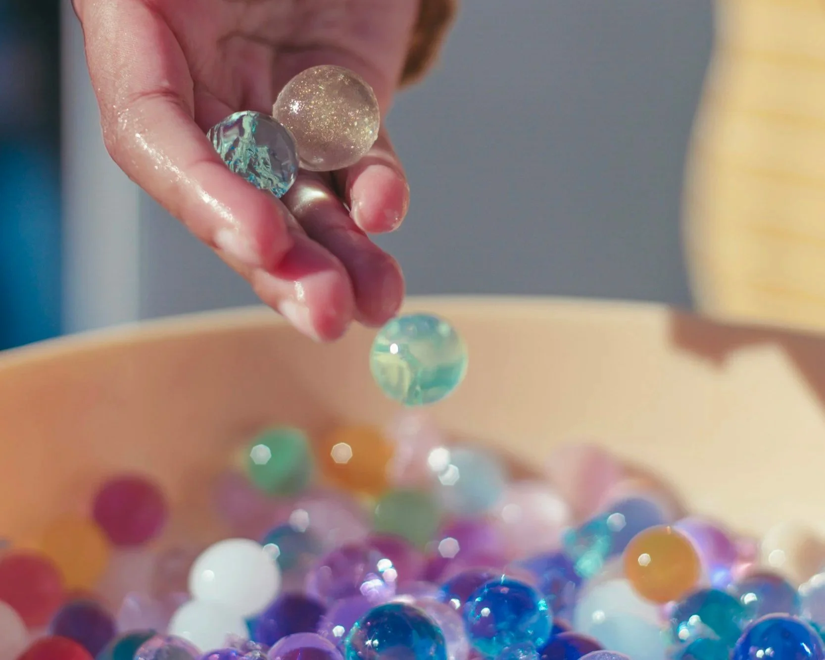 A hand putting sensory water beads into a round container. Focuses on sensory input, sensory needs, and self-regulation.