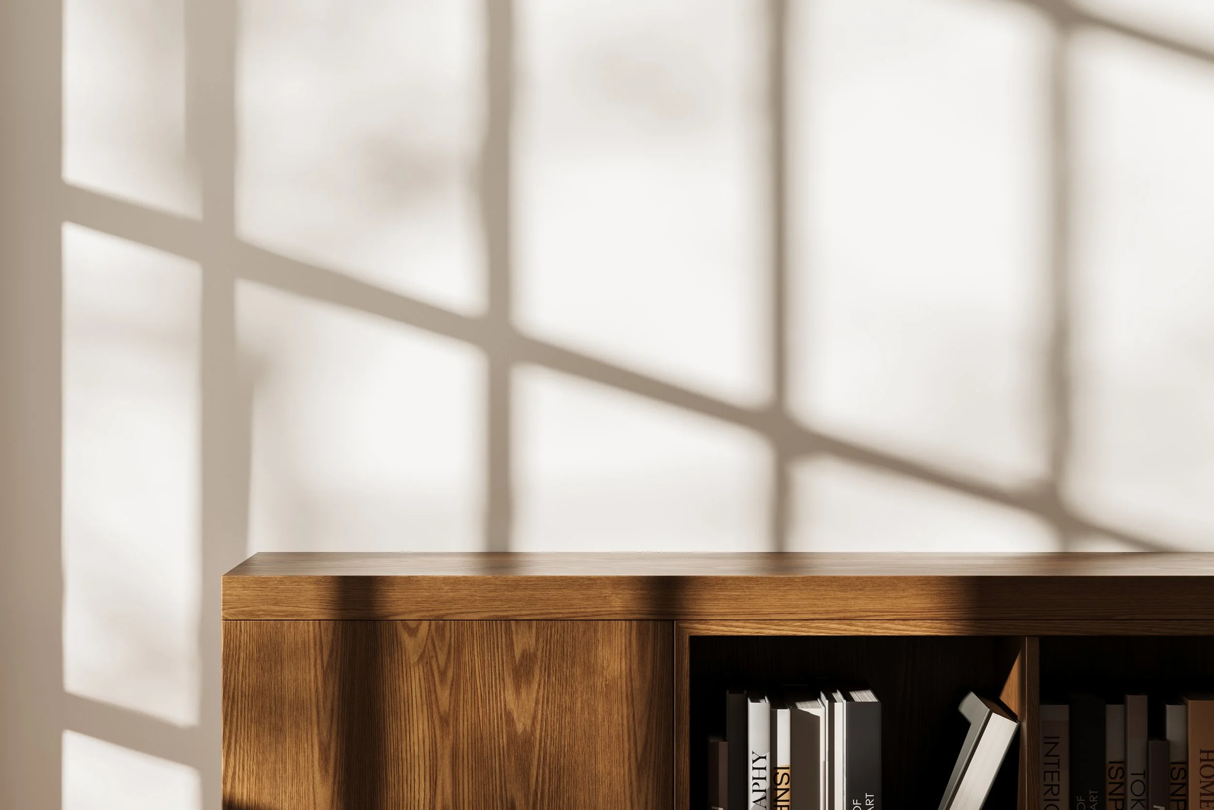 A wooden bookshelf with books on it and shadows of window panes cast on the white wall behind it.
