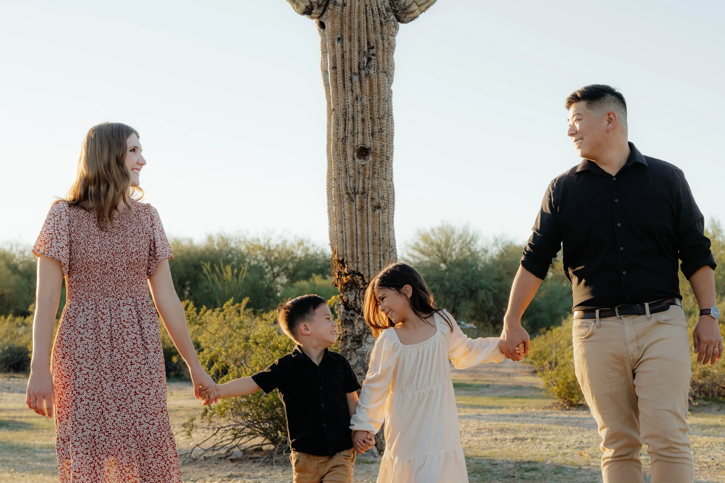A family holding hands and smiling outdoors with a cactus tree in the background during sunset.