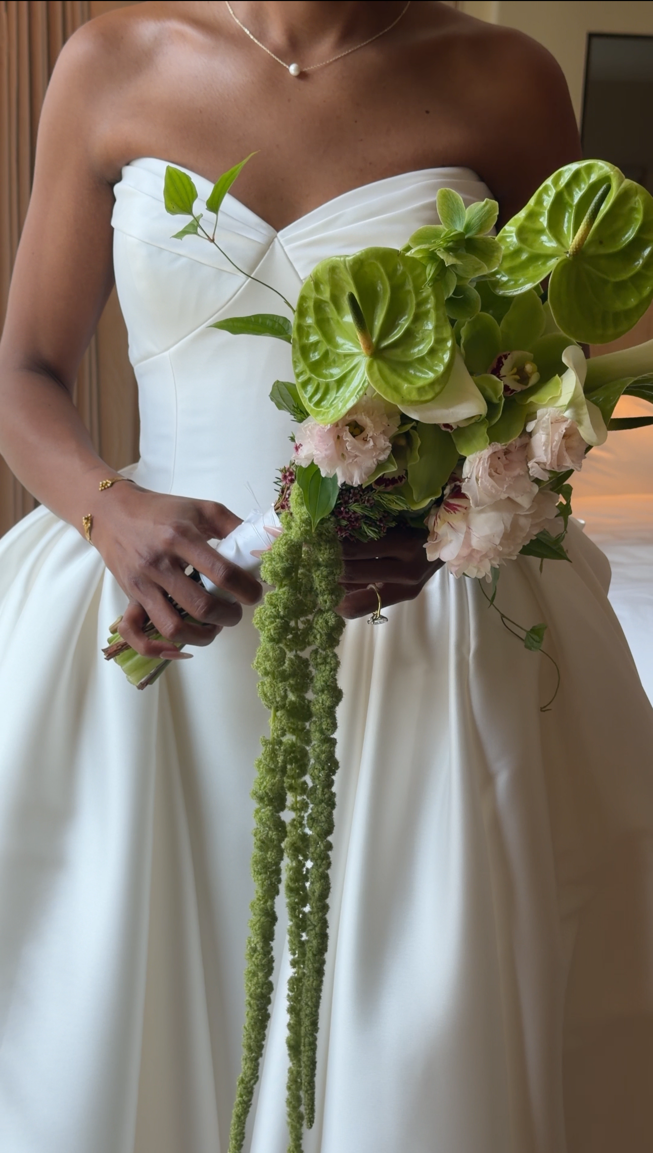 A woman in a white strapless dress holding a bouquet of green and pink flowers.
