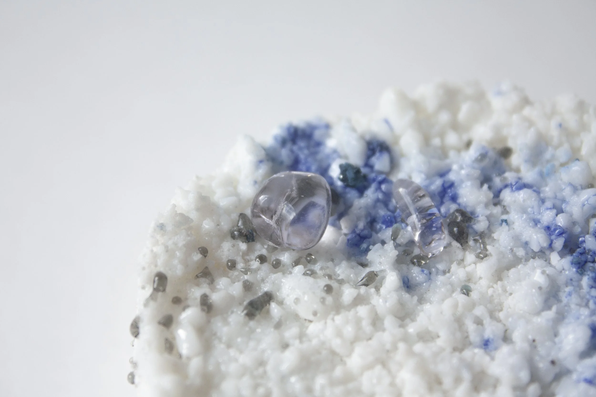 Close-up of a textured surface with small white, gray, and blue particles, some appearing to be small rocks or crystals.