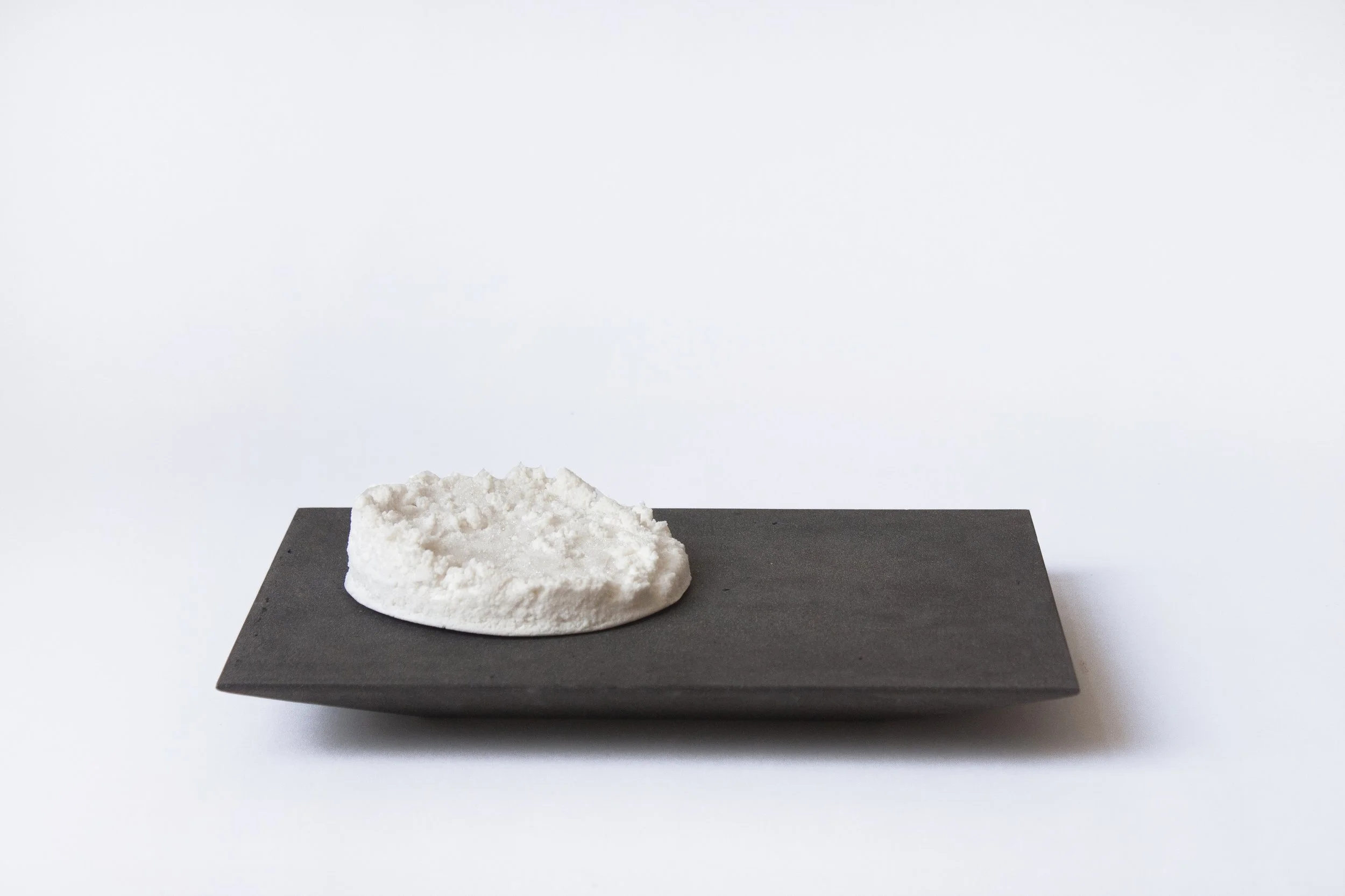 A white, textured rock or mineral specimen placed on a black rectangular base against a plain white background.