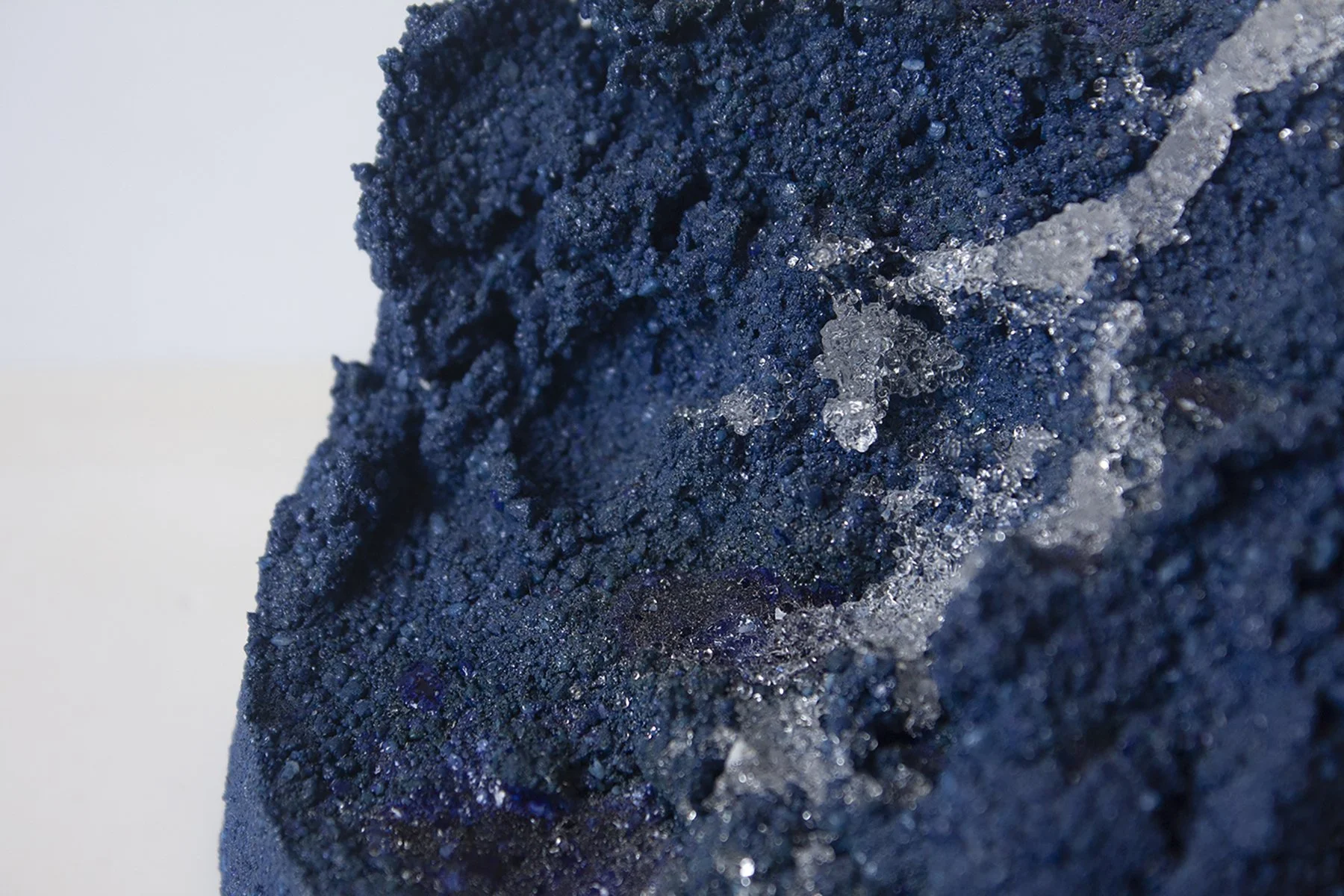 Close-up of a textured, dark blue surface with shiny, crystalline ice formations and a streak of trapped ice crystals.