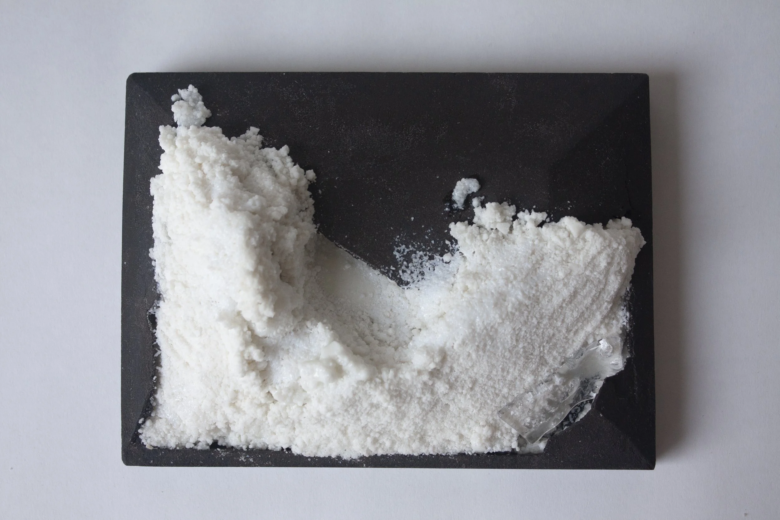 Powdery white substance on a black rectangular slate with a black background.