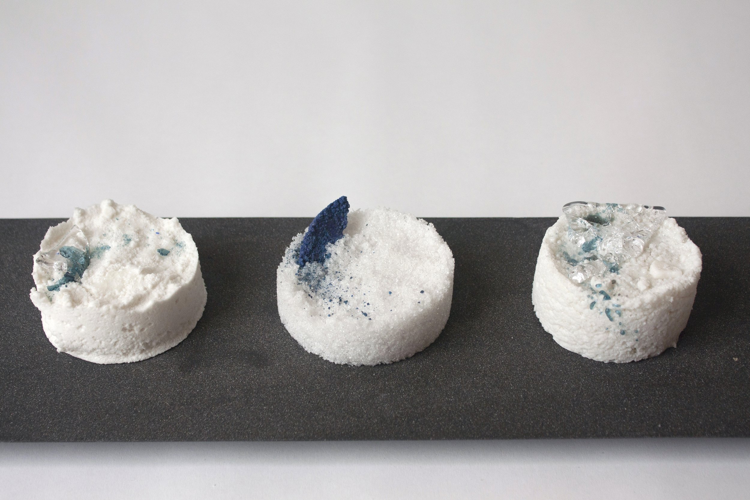 Three white confectionery marshmallows decorated with blue and silver sprinkles and gel.