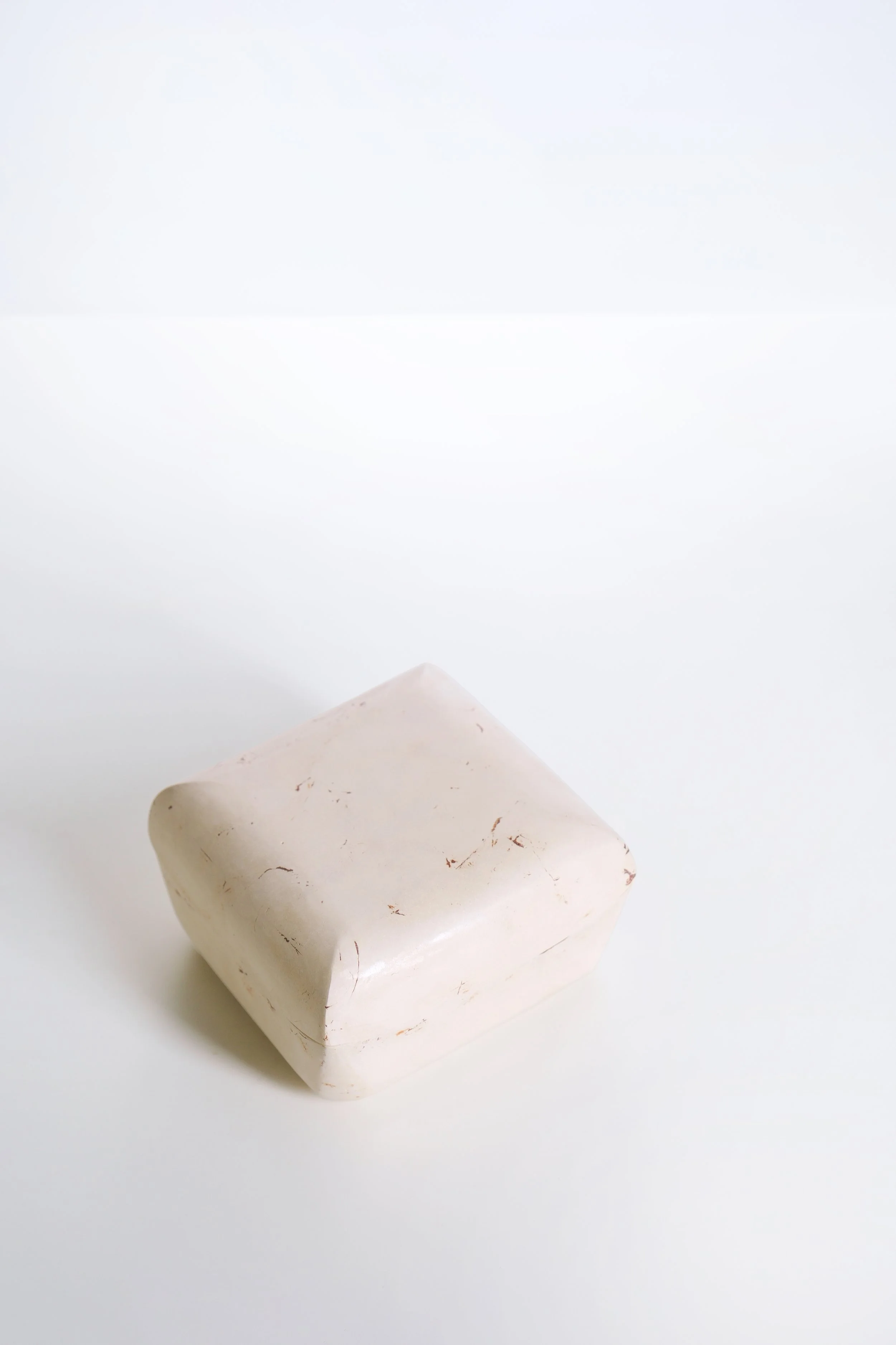 A white wax candle with subtle brown markings on a white surface.