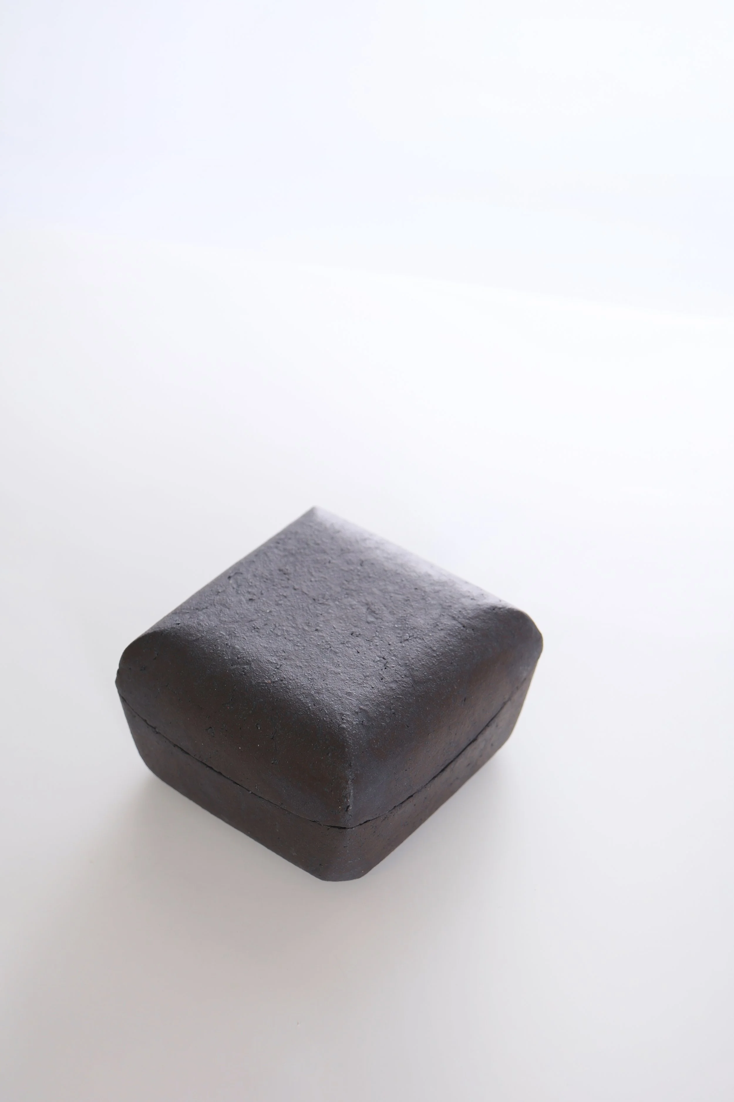 A black, square-shaped piece of chalk on a white surface with a plain white background.