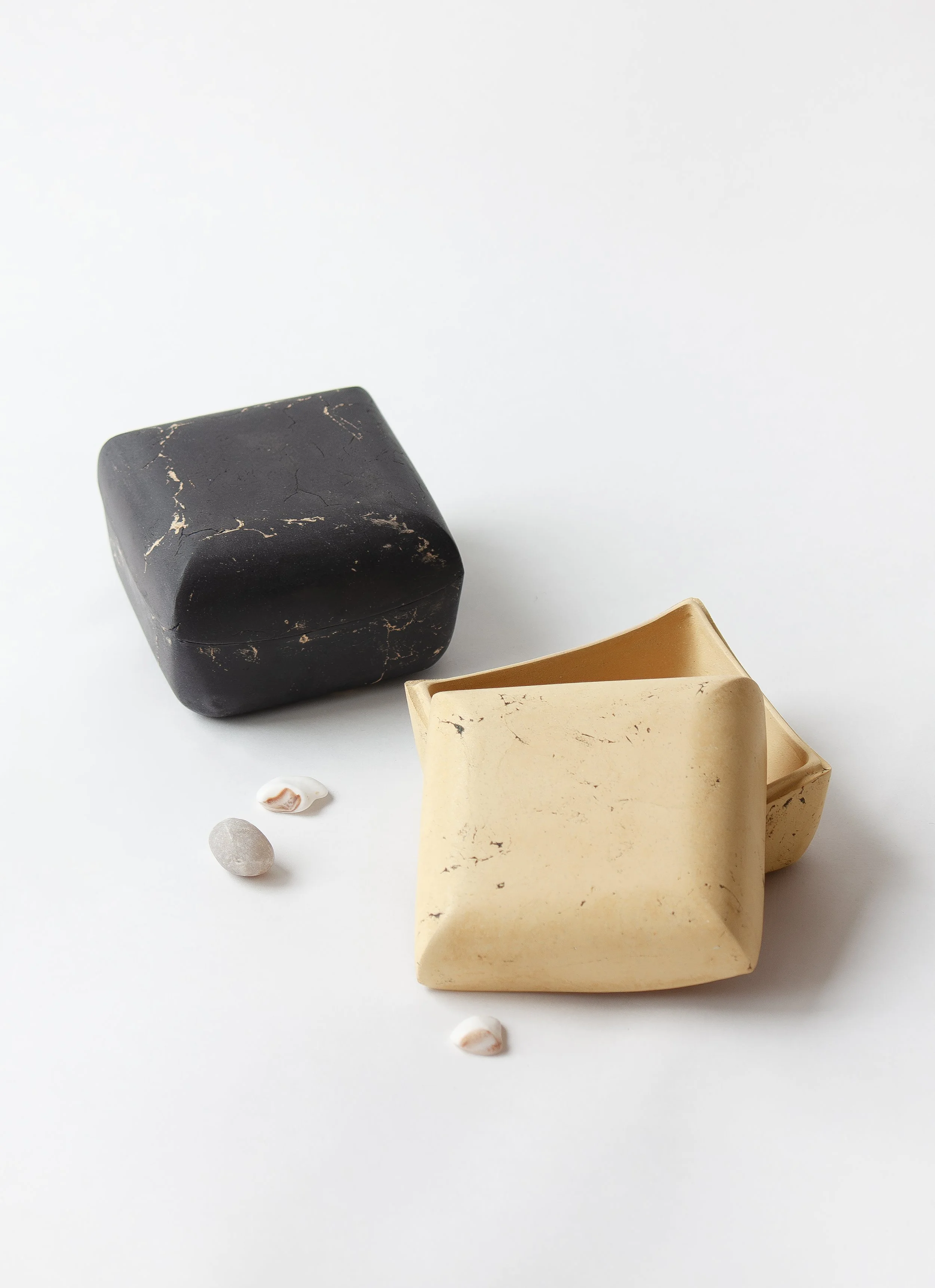 Three soaps, one black, one beige, and one cream-colored, with small seashells on a white background.