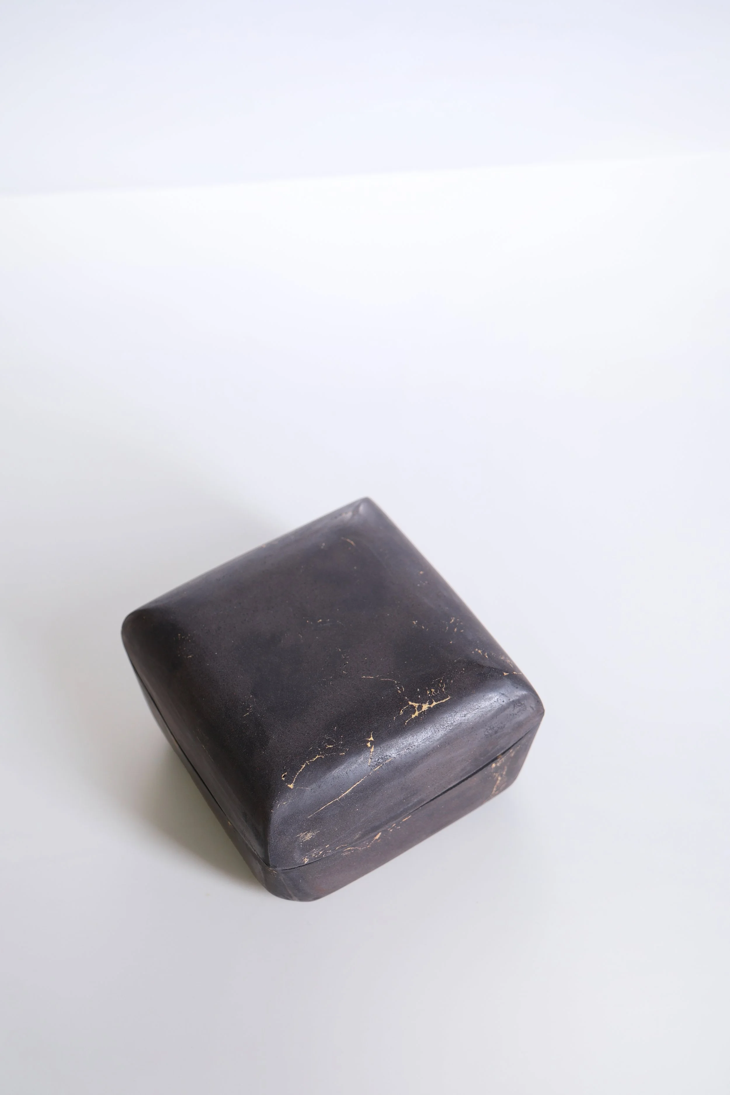 A black marble cube with white and gold veining, resting on a white surface.