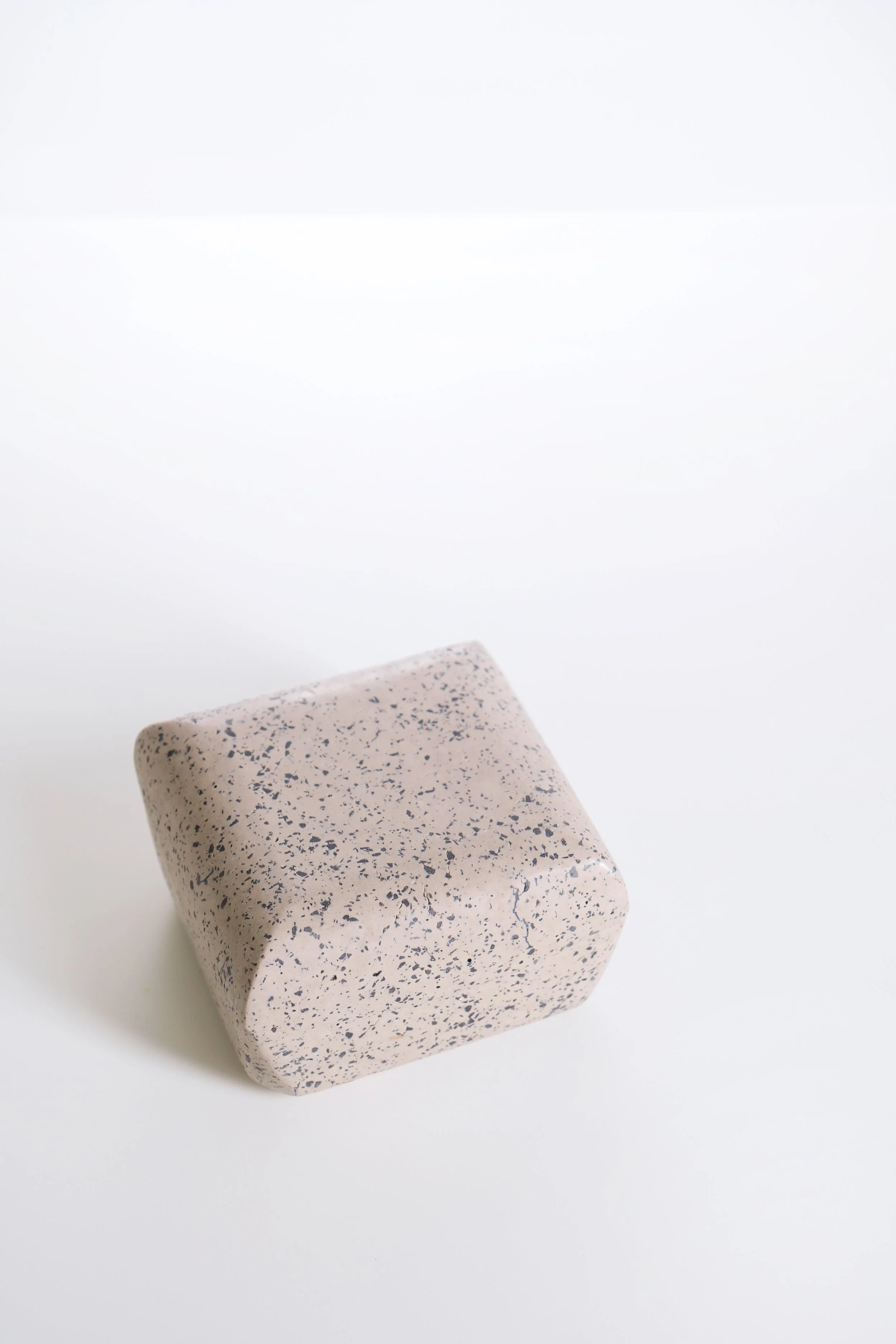 A square-shaped object with a speckled pattern in shades of beige and dark blue, placed on a white surface.