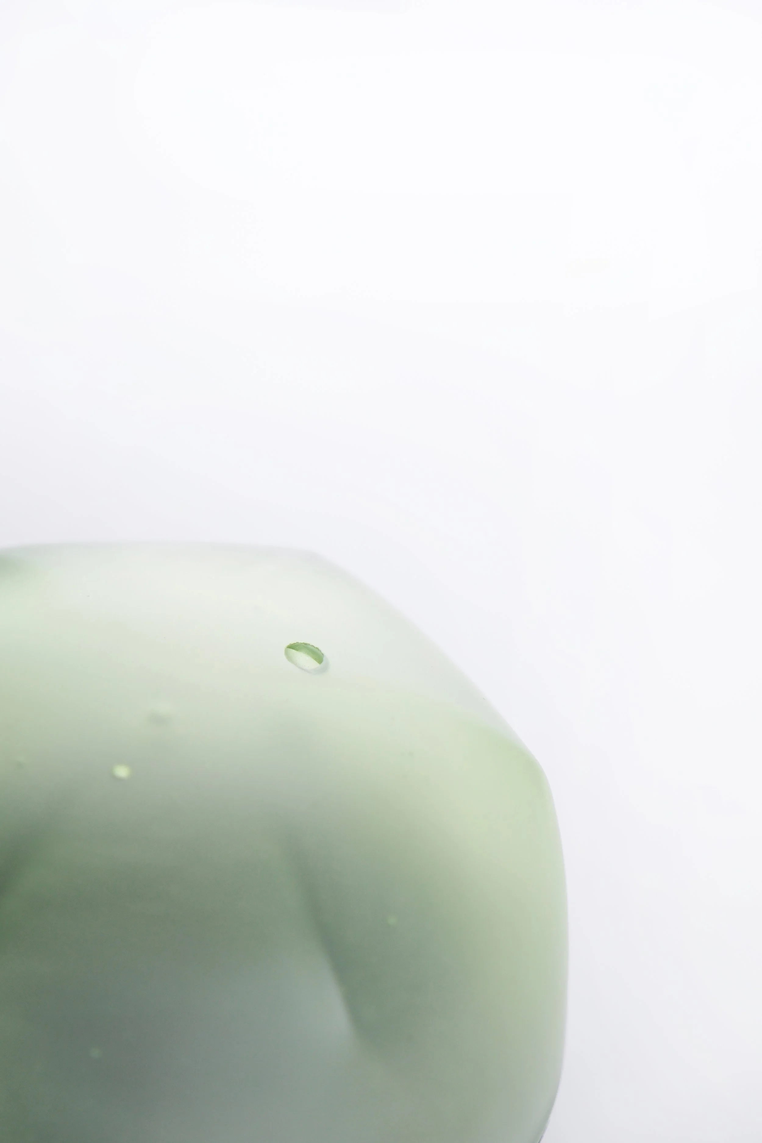 Close-up of a white ceramic teapot with green liquid inside and a small droplet on the surface.