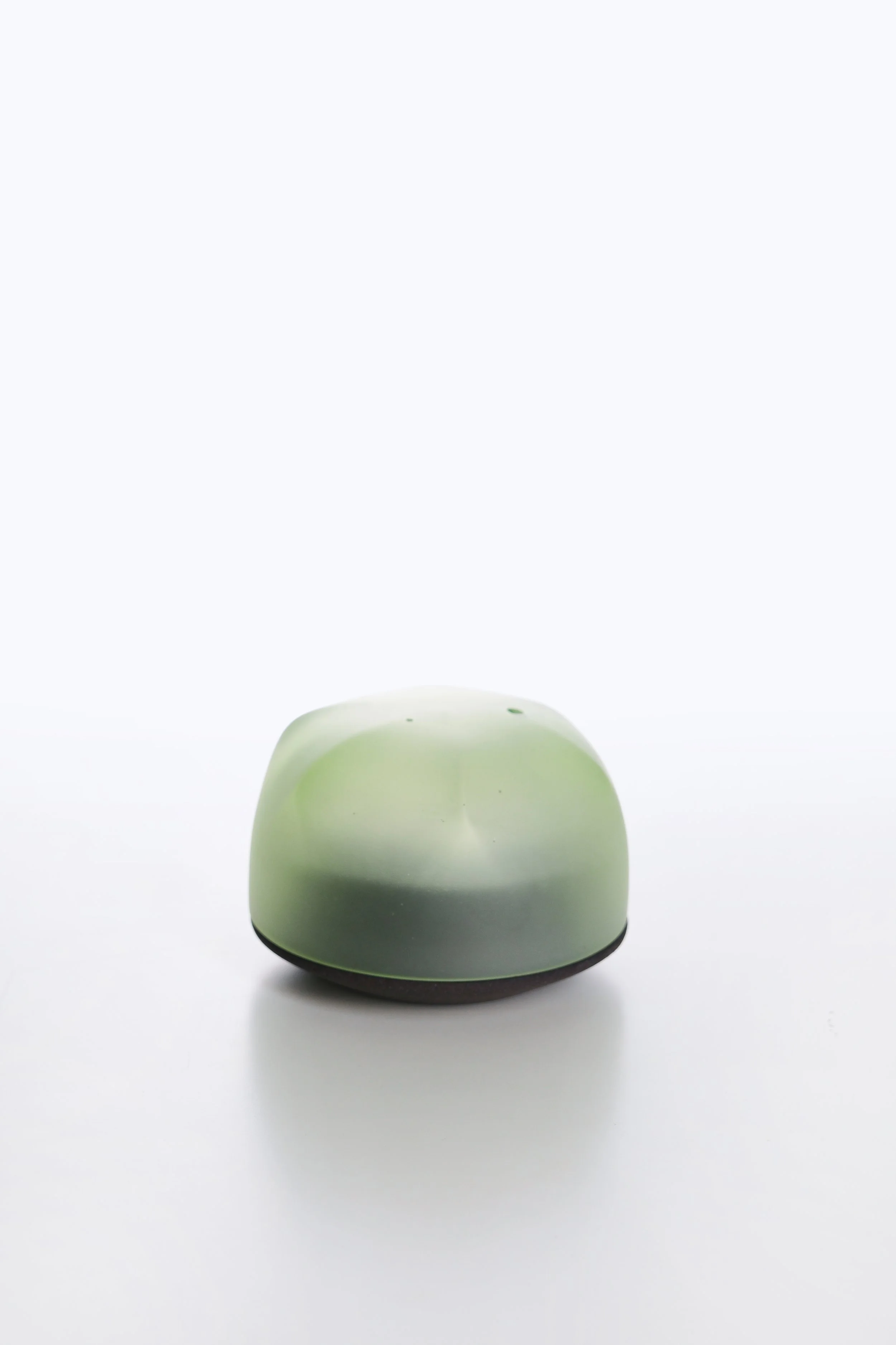 A small, rounded, light green object with a smooth surface, sitting on a black base against a plain white background.