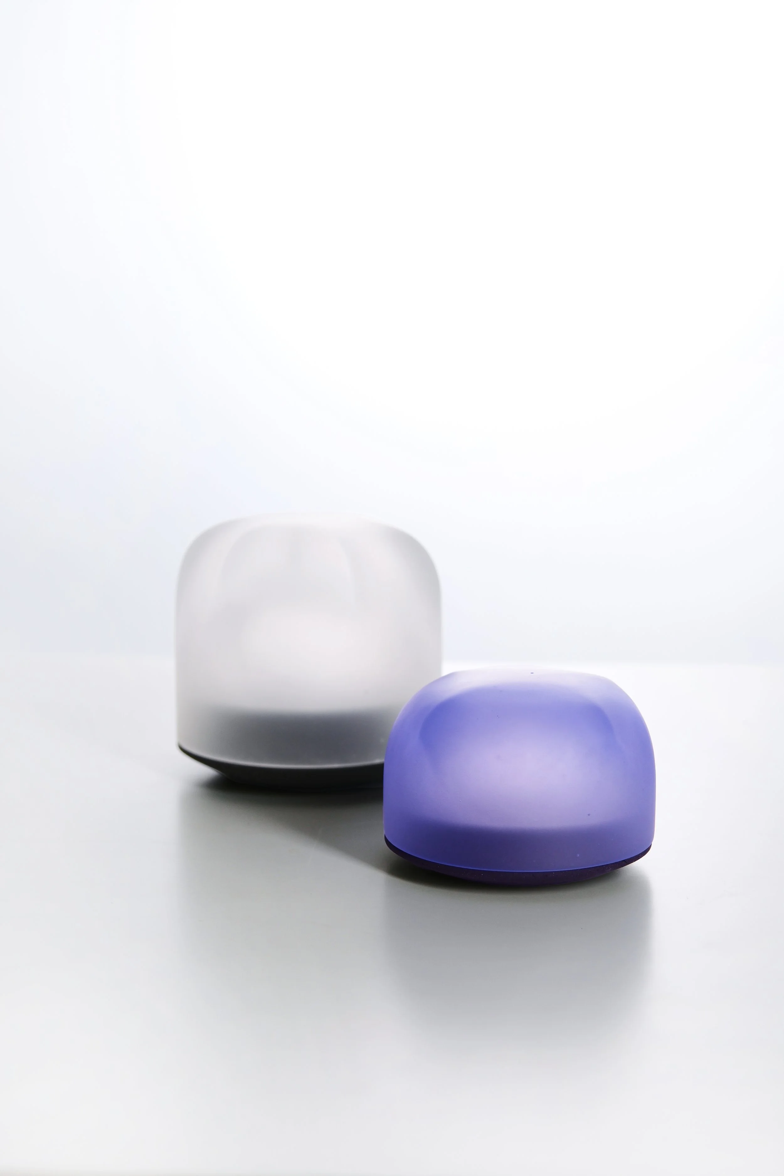 Two modern LED table lamps, one white and one purple, placed on a white surface against a white background, with the purple lamp in the foreground.