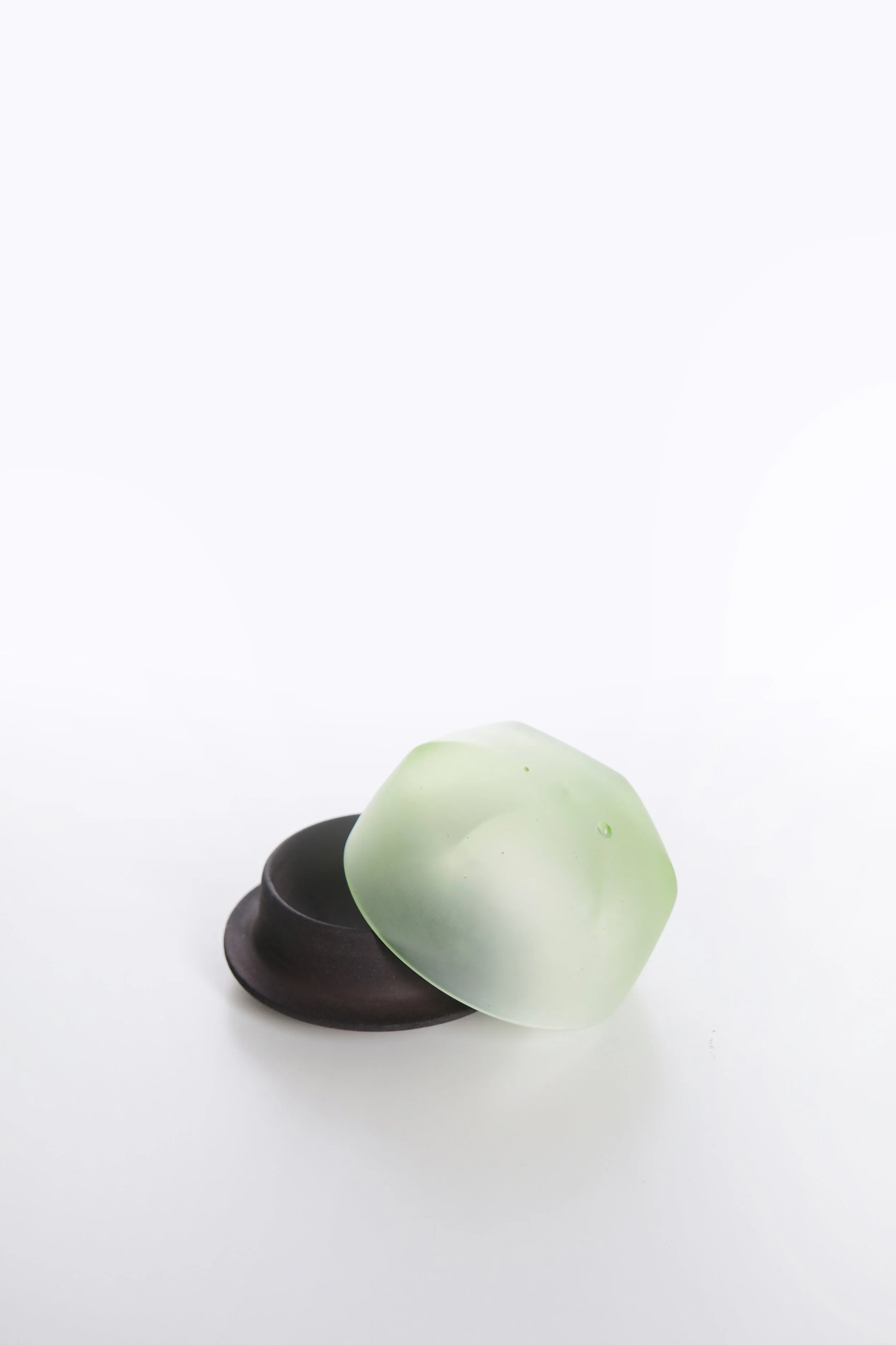 A small black bowl holding a light green cactus with a smooth surface and droplets of water, set against a plain white background.
