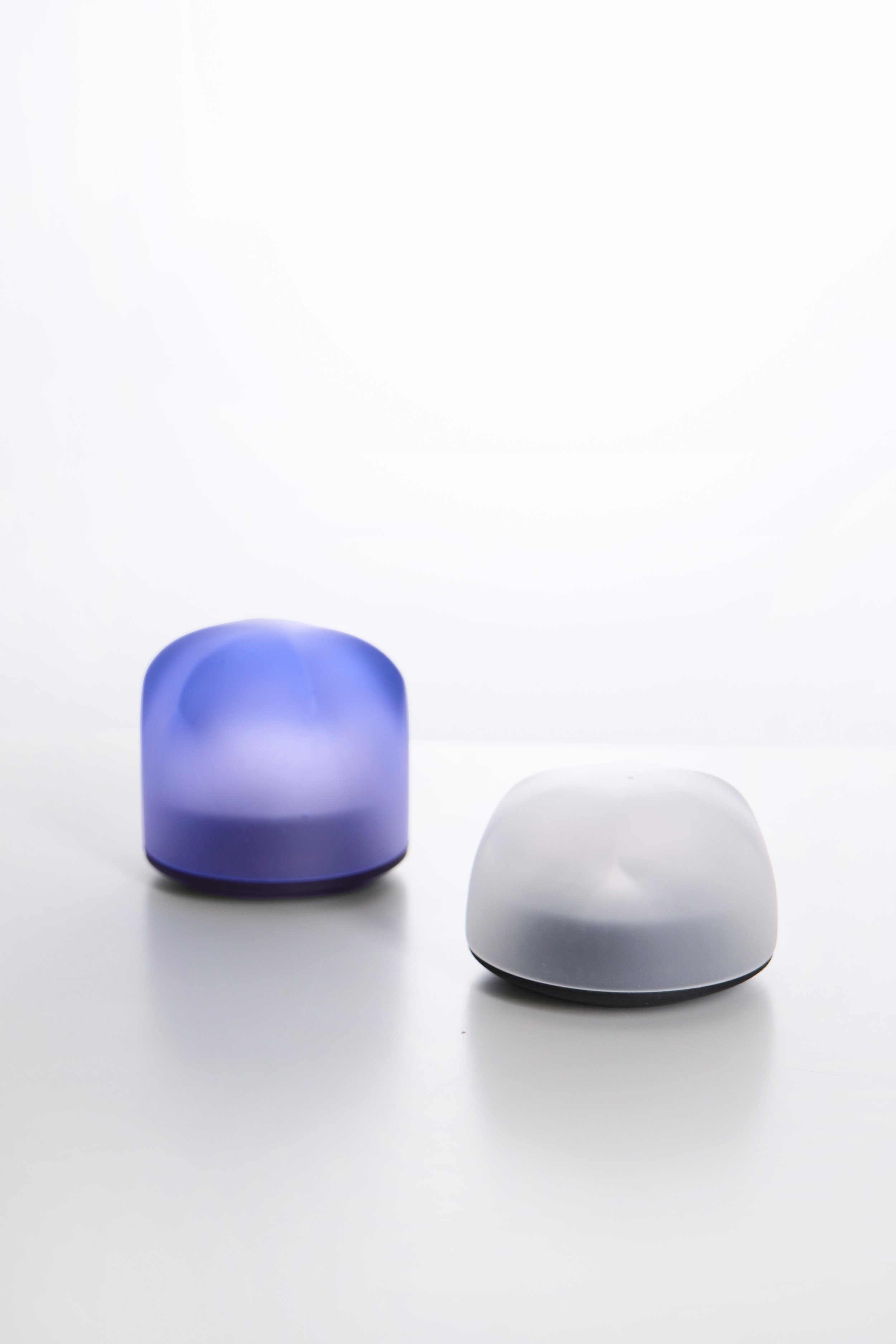 A purple and a white apple-shaped wireless speaker on a white surface against a white background.