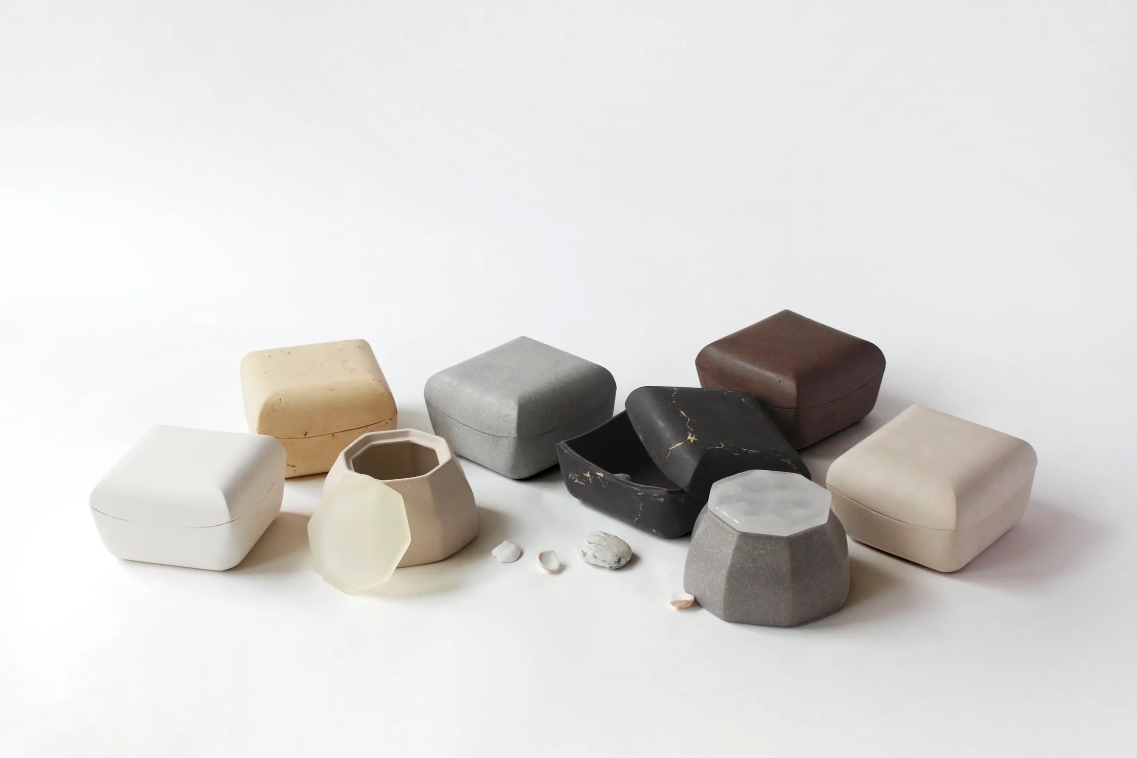 Various stones and ceramic objects in different shapes, colors, and sizes arranged on a white surface against a plain white background.