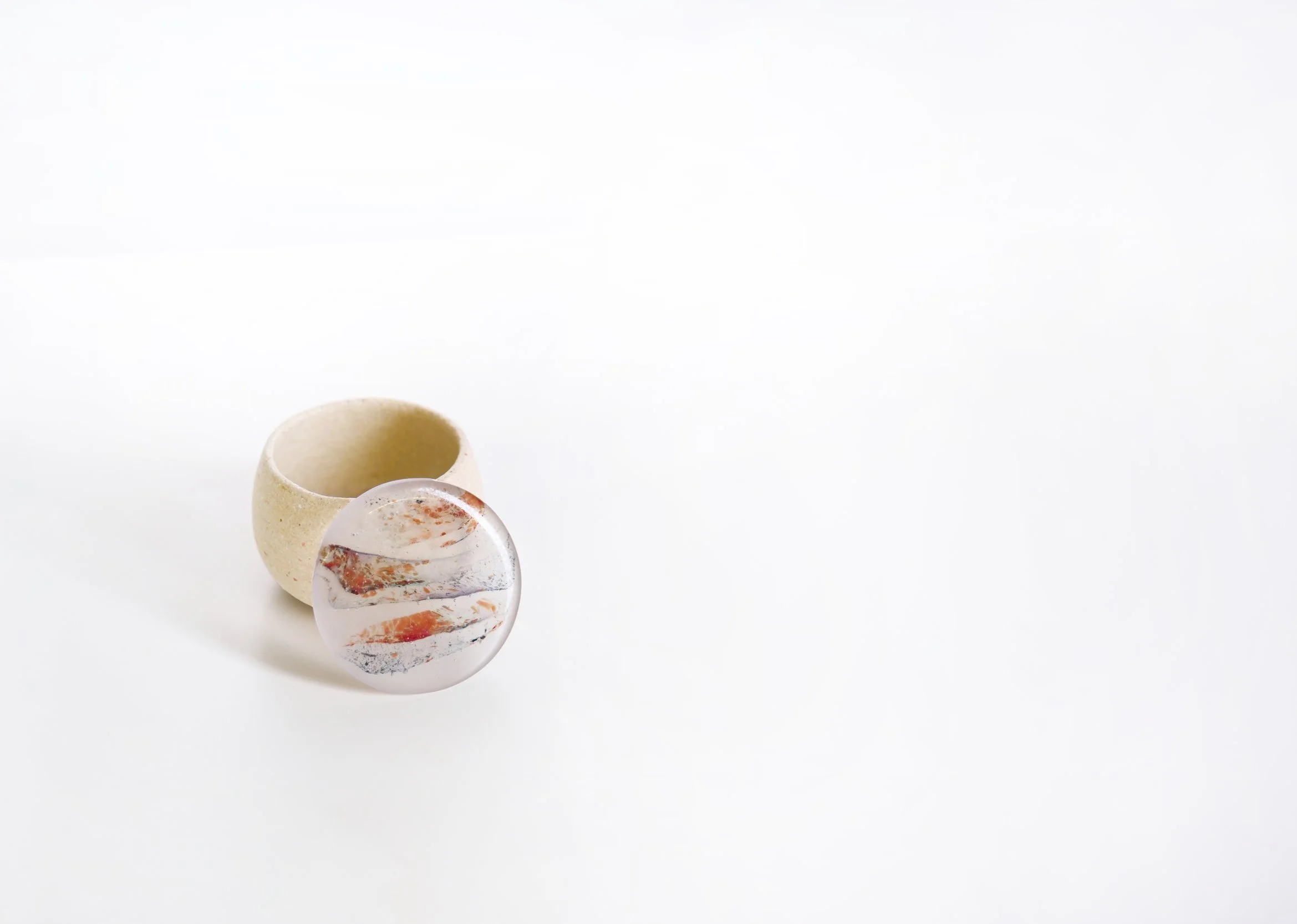 Close-up of a marble with orange, black, and white swirls, and a small ceramic cup with a rounded opening on a white surface.