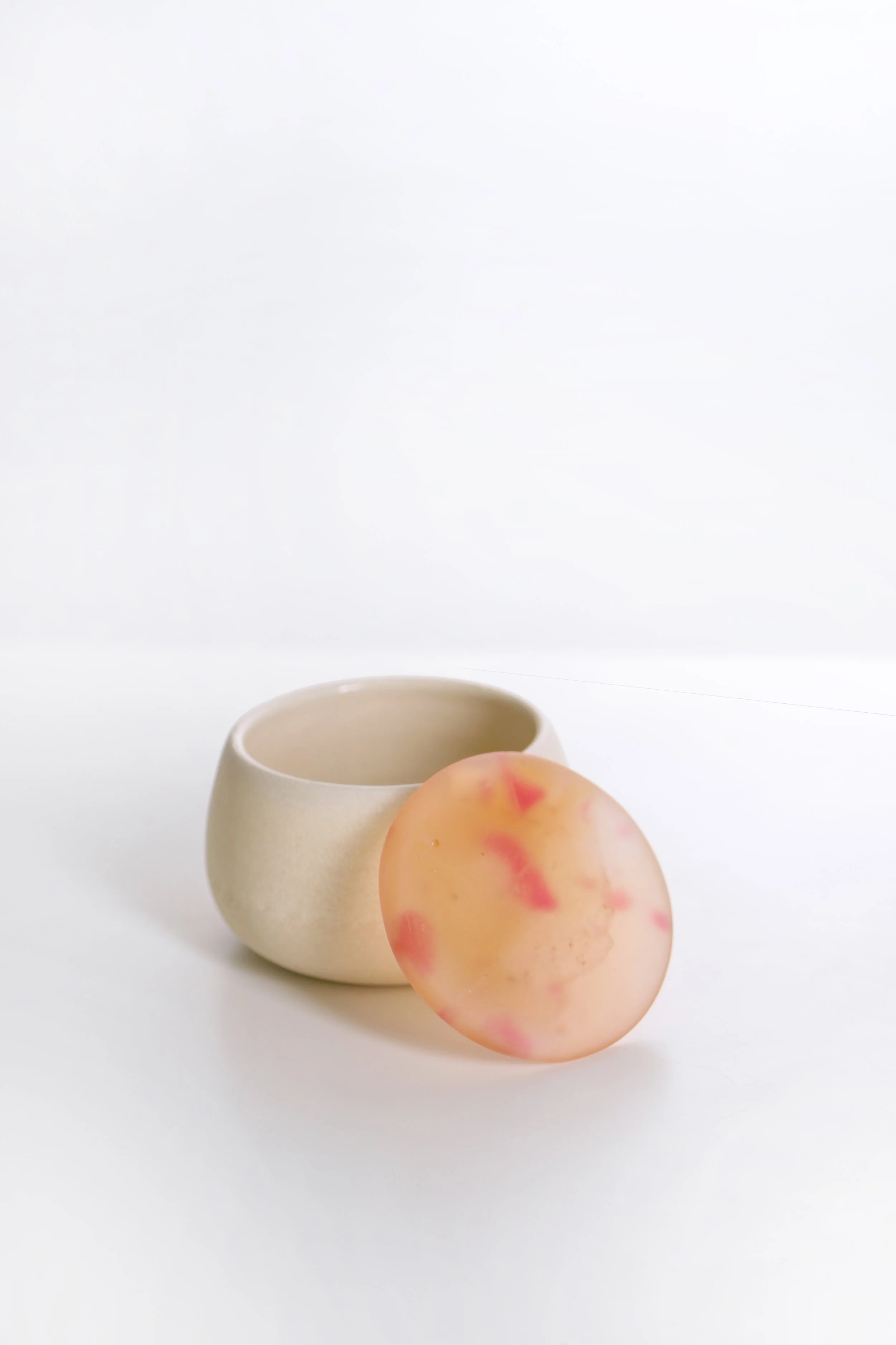 A peach-colored stone with pink and yellow marbling, a small beige ceramic cup, and a white background.