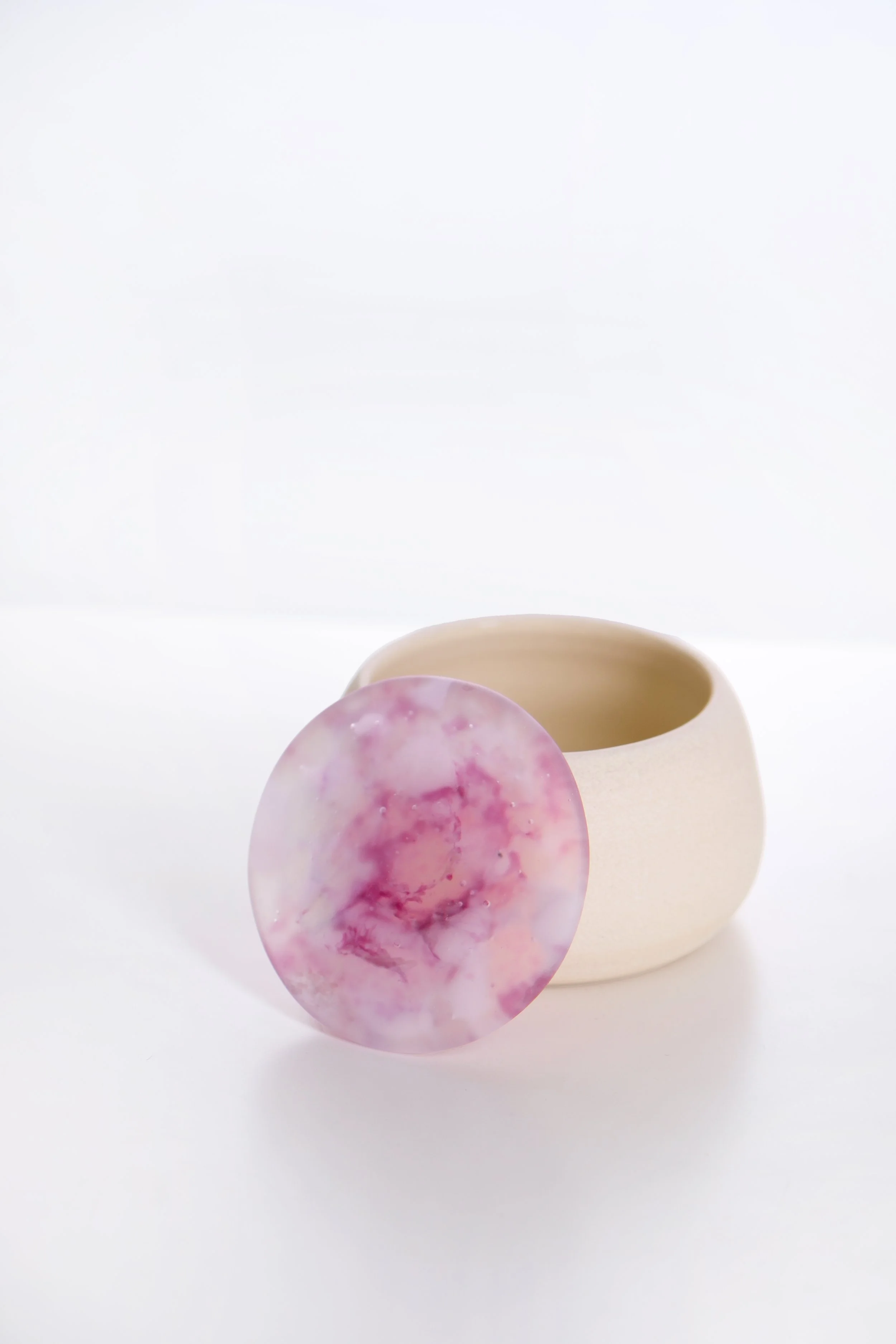 A beige ceramic cup with a pink and purple marble-patterned circle leaning against it, set against a plain white background.