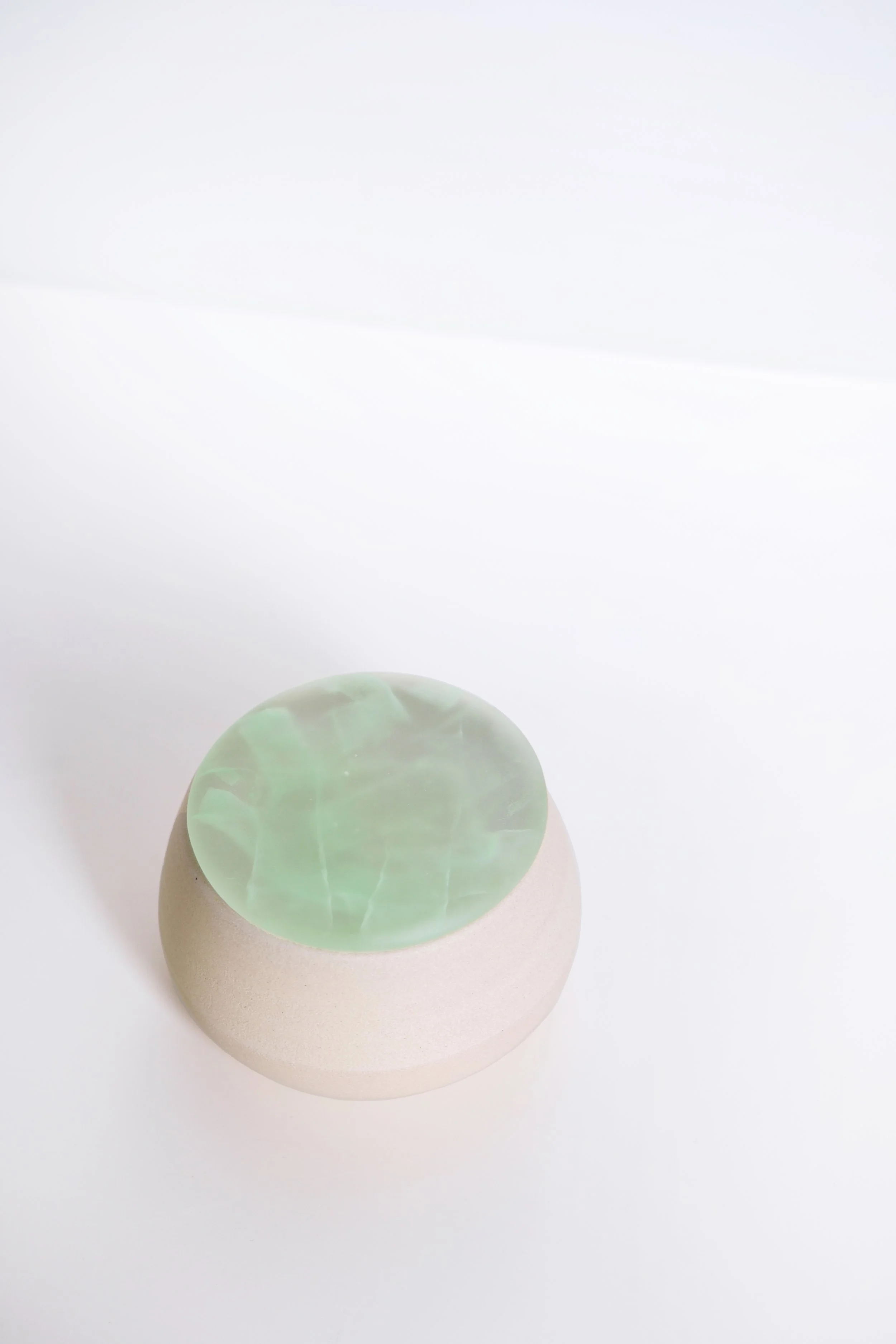 A smooth, round pale pink stone with a large, translucent, greenish-white marble on top of it, against a plain white background.