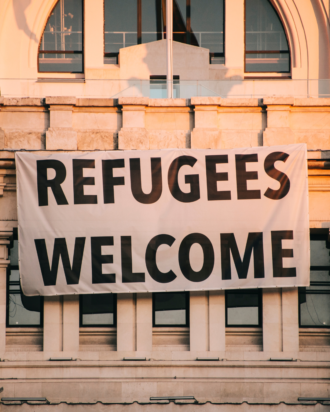 A large banner on a building with the words 'Refugees Welcome' in bold black letters.