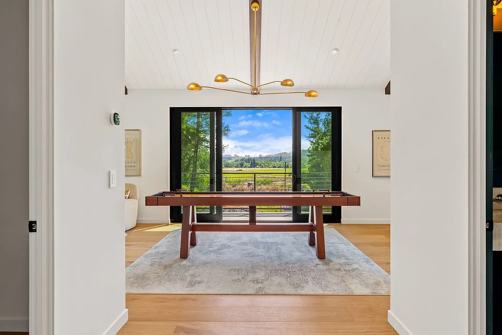 View of a bright room with large sliding glass doors facing a lush green landscape, featuring a foosball table in the center.