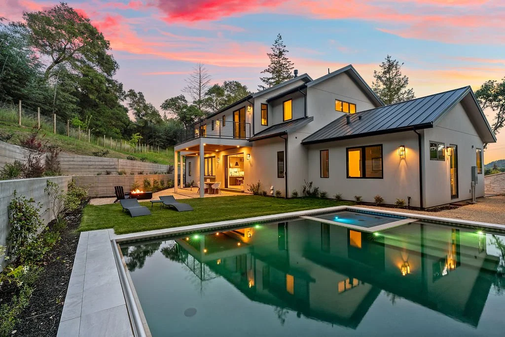 Modern house with a pool in backyard during sunset, with outdoor seating and fire pit.