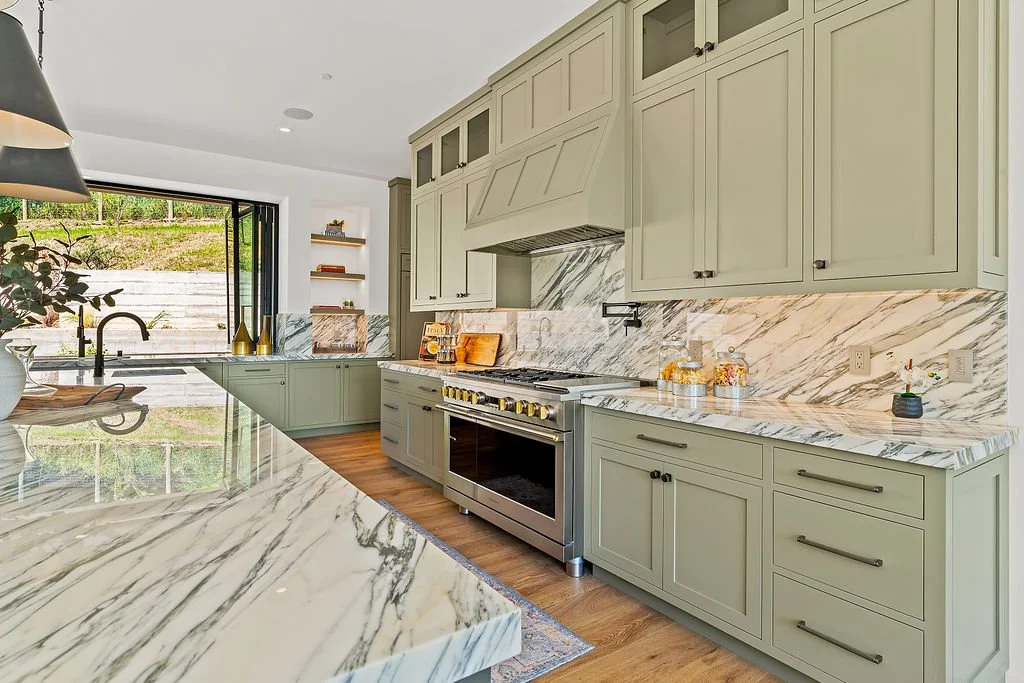 Modern kitchen with green cabinetry, marble countertops, and wood flooring.