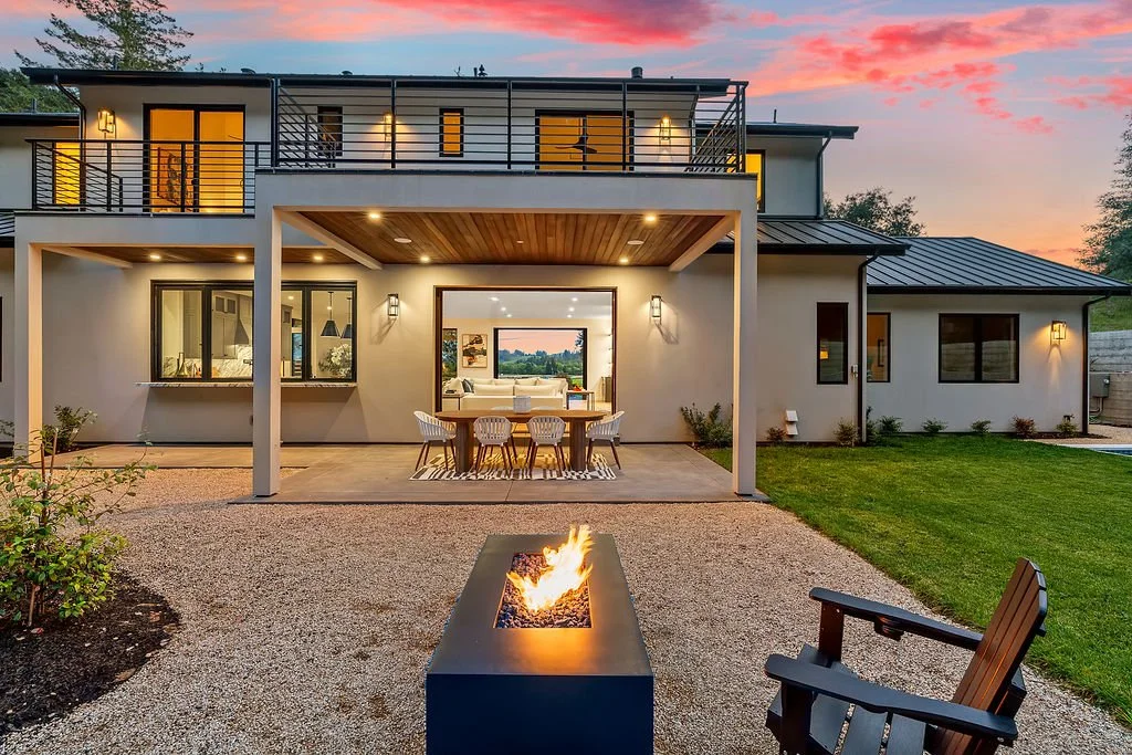 Modern two-story house with outdoor patio, fire pit, and lawn at sunset.