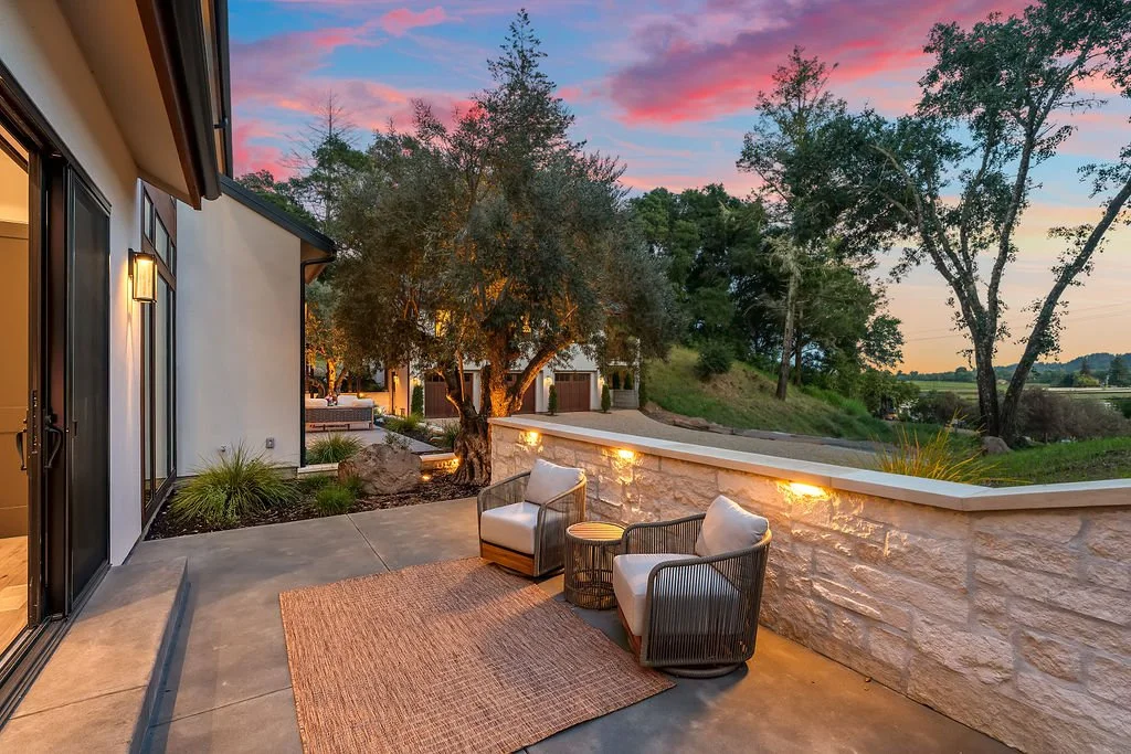 A cozy outdoor patio with two chairs and a small table, overlooking a scenic landscape with trees at sunset.