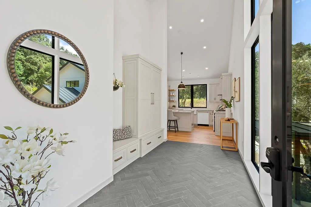 Modern interior hallway leading to kitchen, with white walls, large windows, and gray herringbone tile floor.