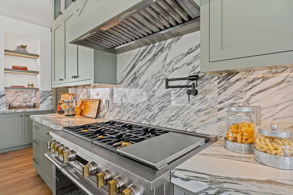 Modern kitchen with marble backsplash and countertops, stainless steel stove, and glass jars of pasta on the counter.