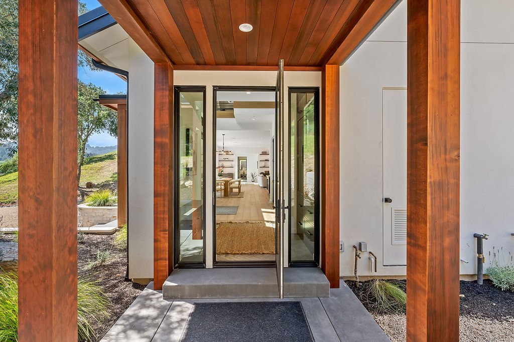 Entryway with glass doors leading into a modern, open-concept home with wood and white interior design.