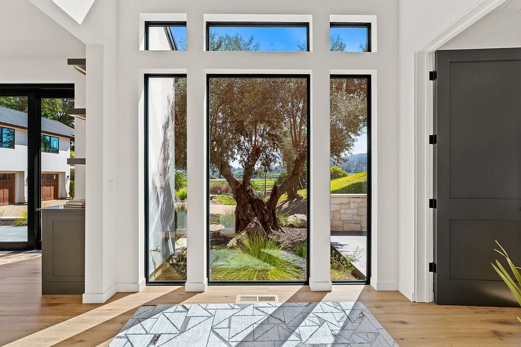 Interior view of a modern home with large glass doors and windows showing a view of a tree and a grassy landscape outside.