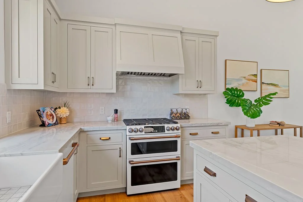 White kitchen with marble countertops, a stove, and wall art with green plant decoration.