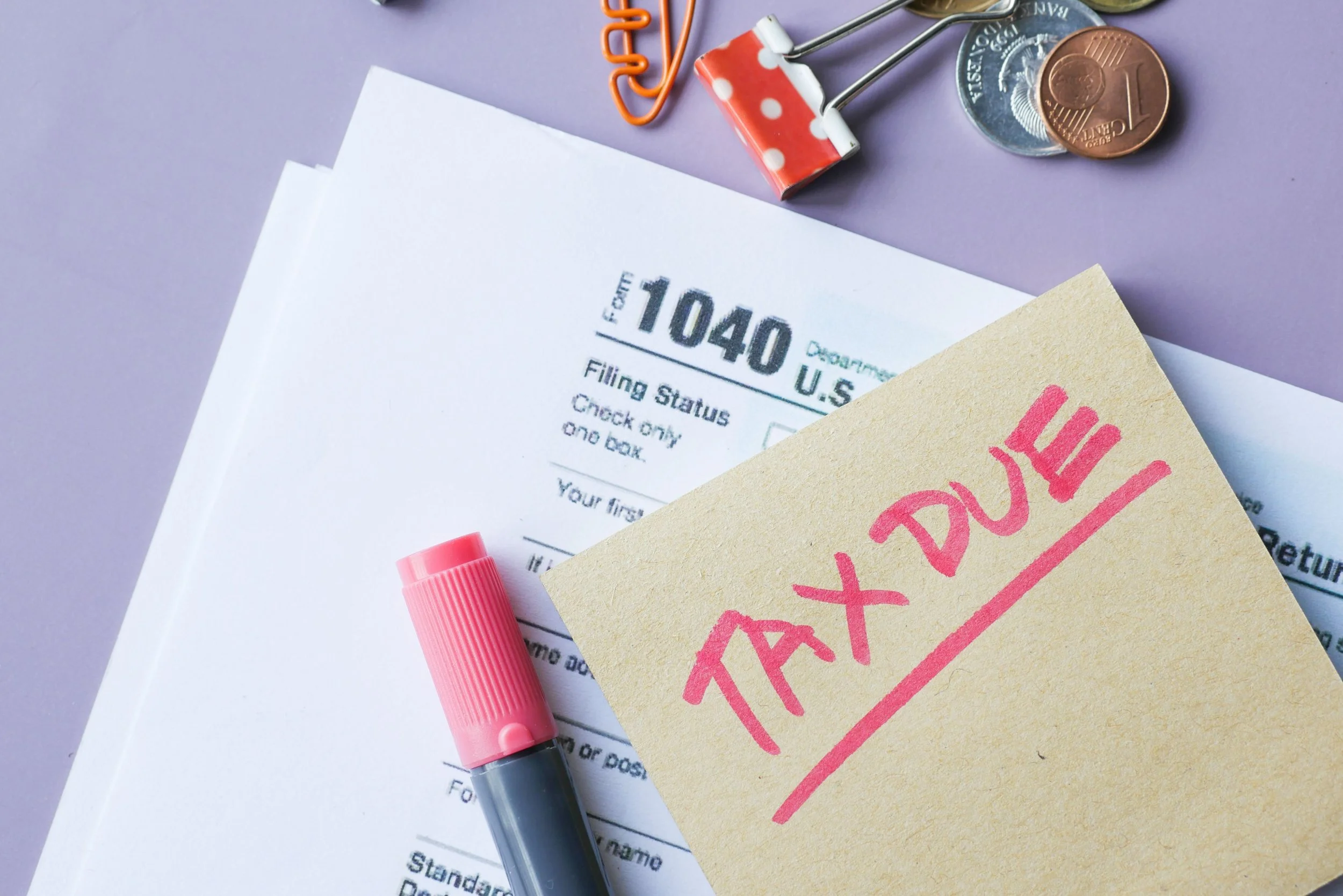 A Form 1040 tax return with coins and paperclips on top, representing the taxable "boot" income that can arise in a 1031 exchange.