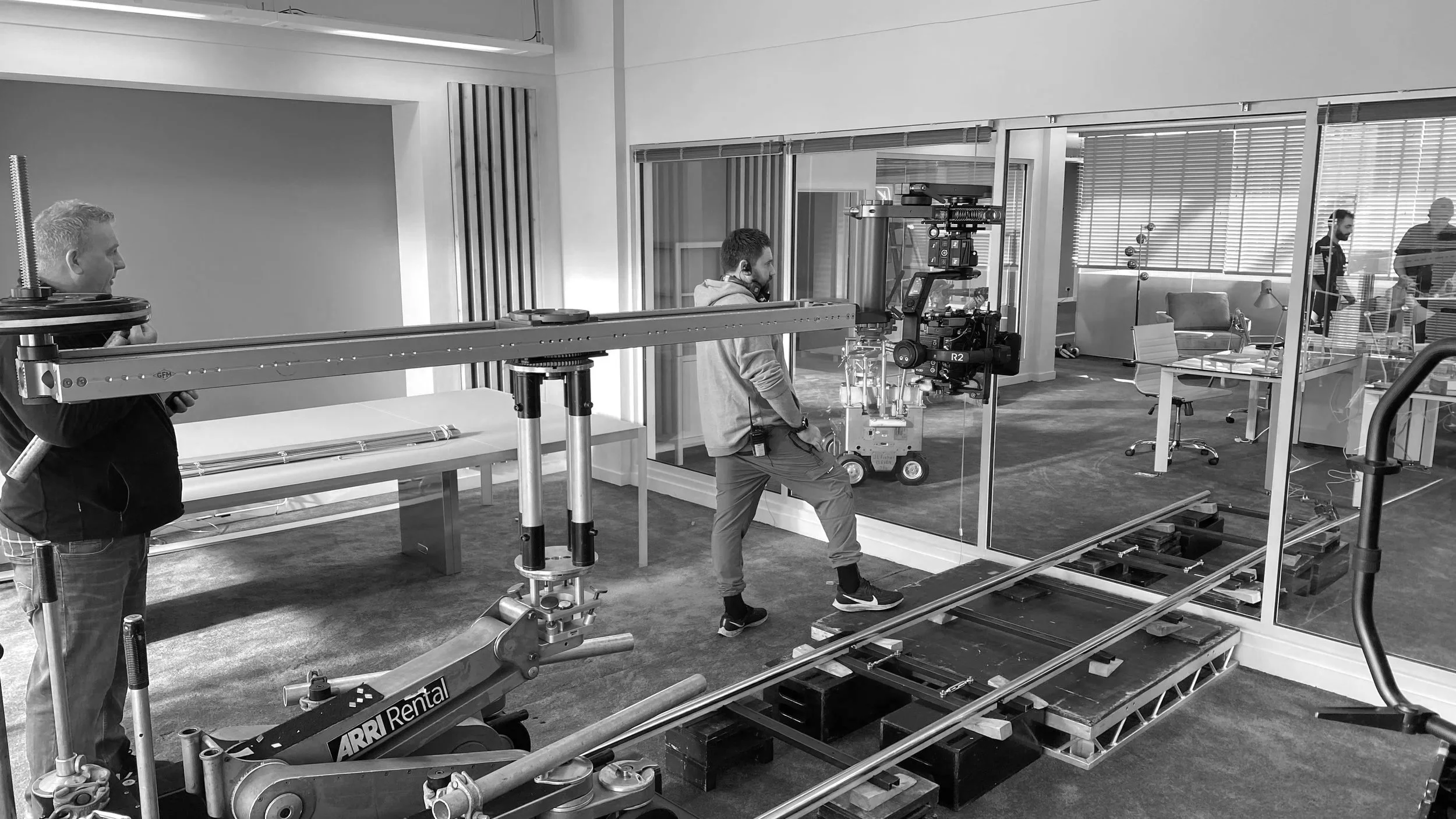 A film crew setting up equipment on a stage with a dolly and track, preparing for a scene shoot in an office space.