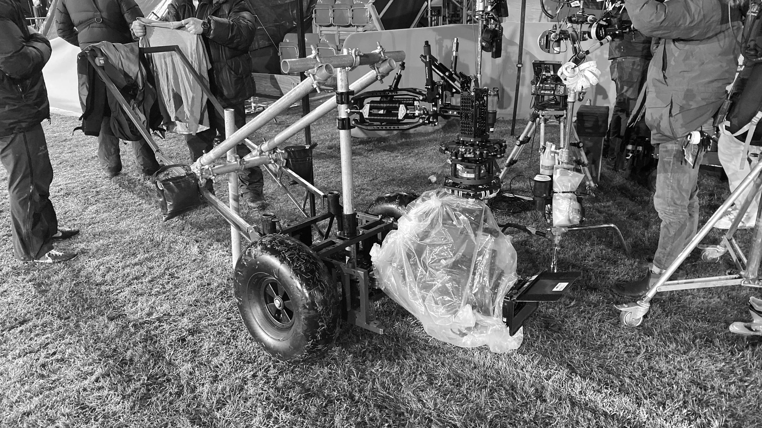 This black and white photo shows a group of people working with a camera rickshaw on a grassy field at night.
