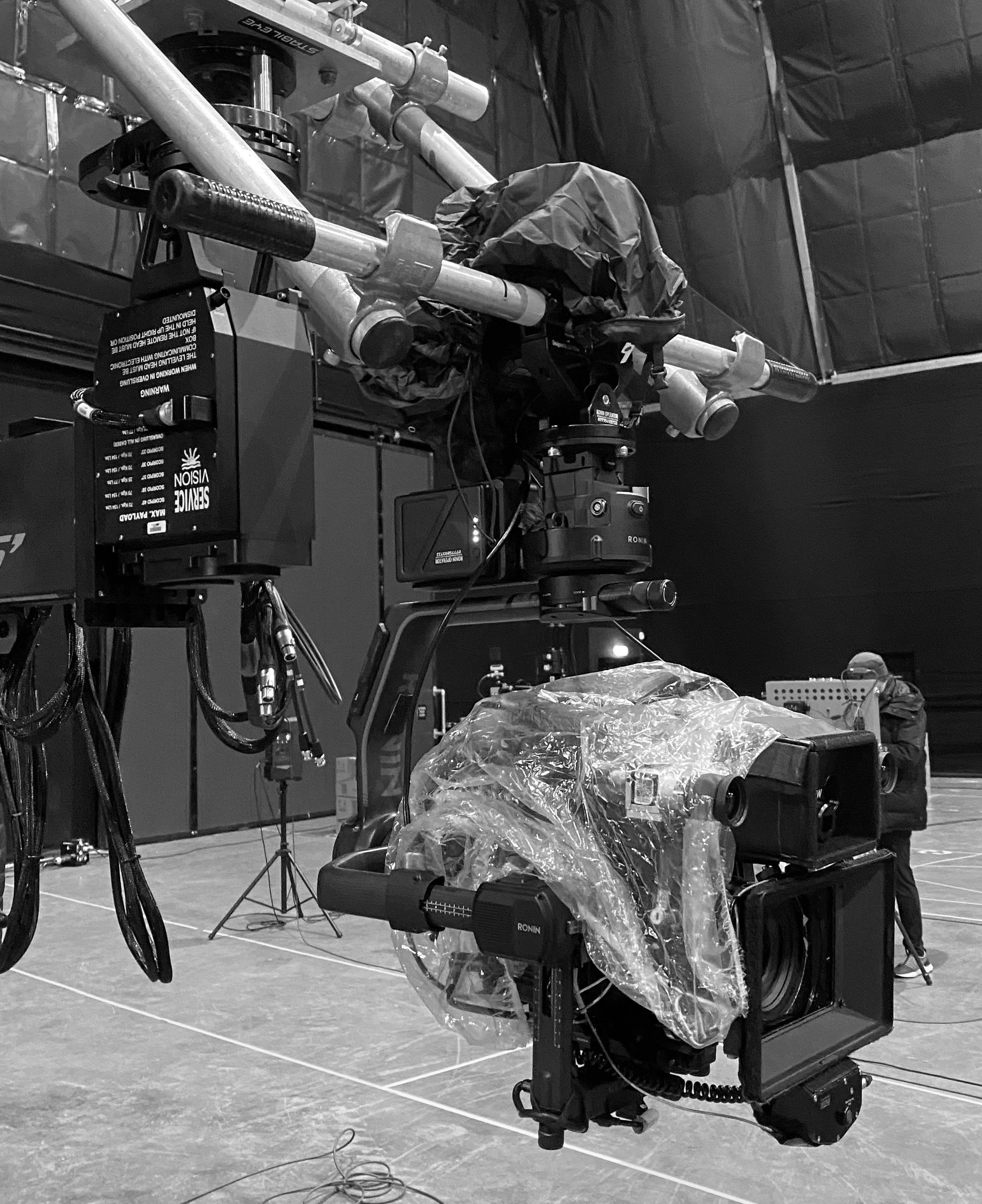 A camera mounted on a complex rig with various components and cables, used for professional filming or broadcasting, in an indoor studio or stage setting.