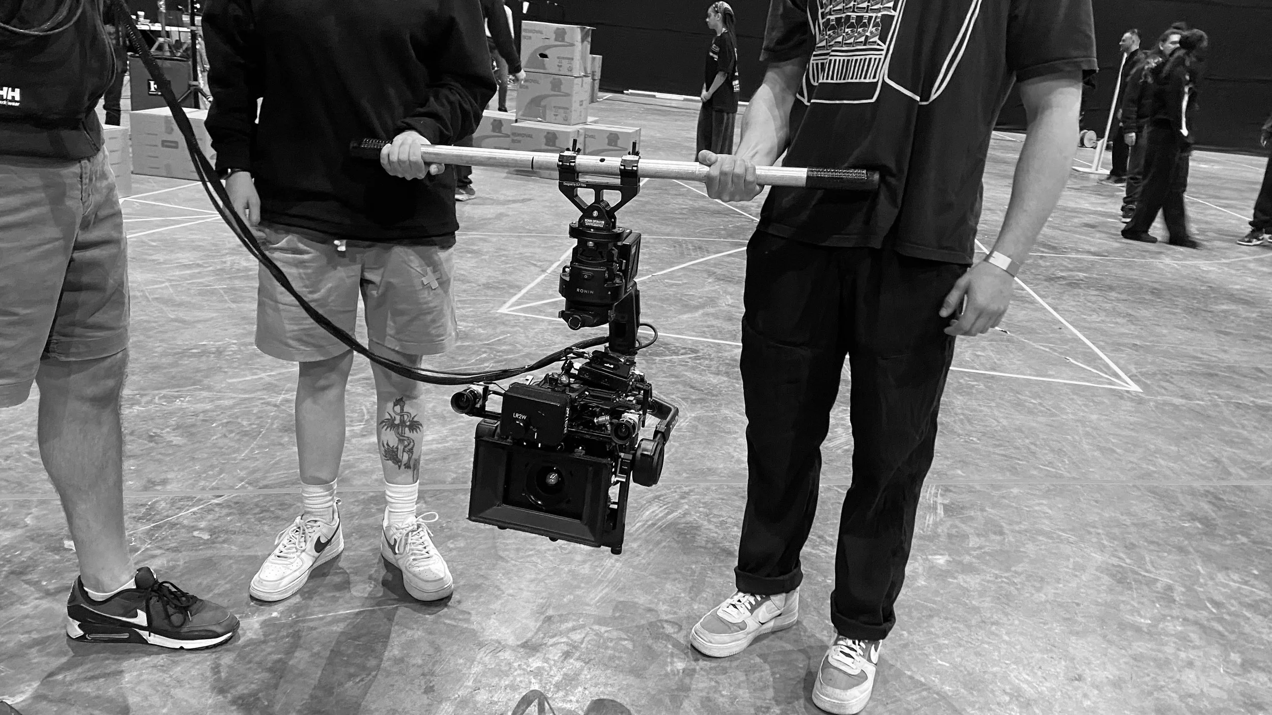Group of people gathered around a camera mounted on a stabiliser in an indoor sports facility or gym.